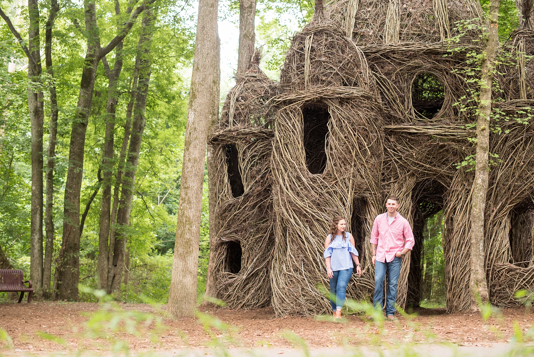 Mikkel Paige Photography photos of an engagement session at Eno Riverwalk in Hillsborough, North Carolina. Picture of the bride and groom walking with a stick art sculpture in the background.