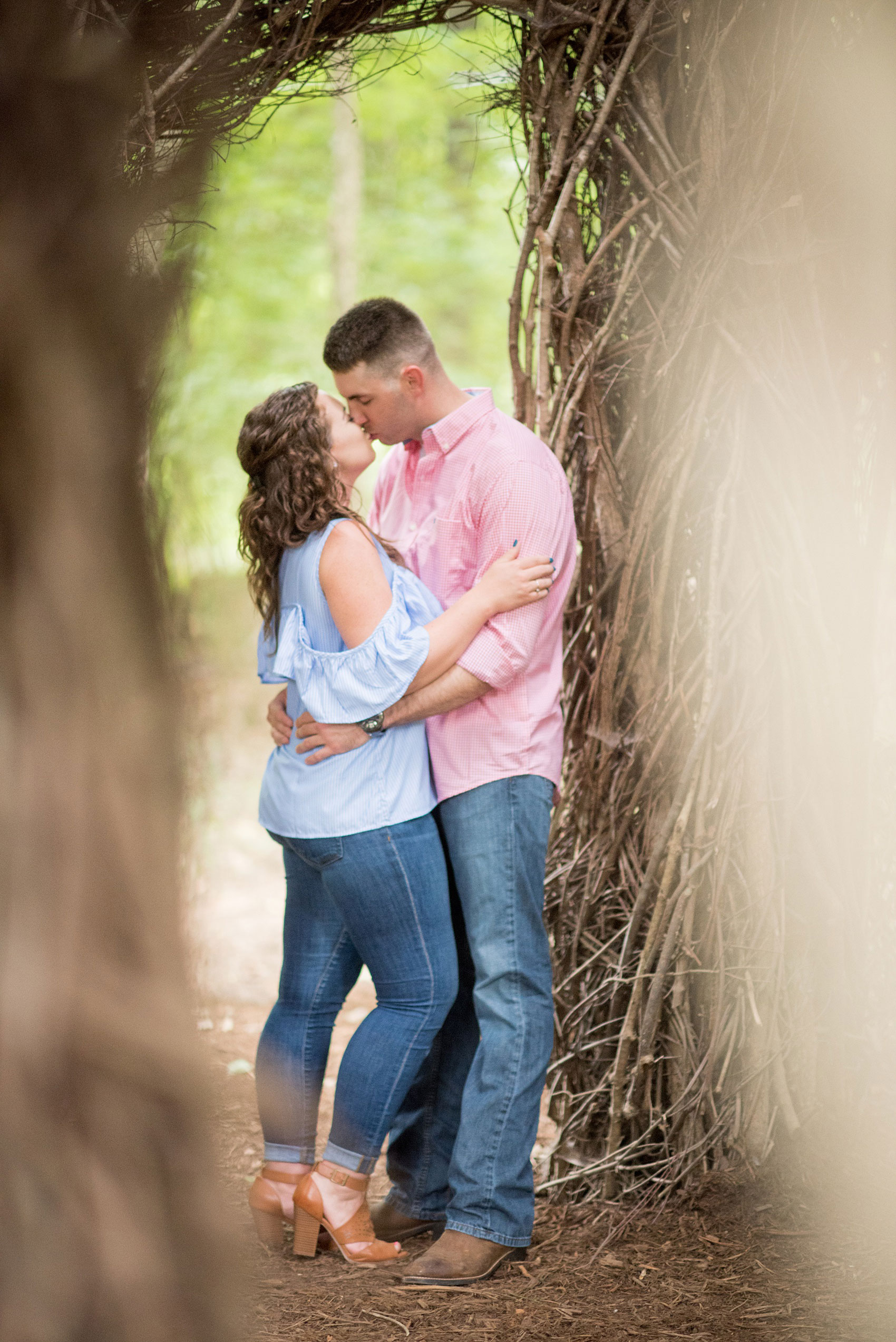 Mikkel Paige Photography photos of an engagement session at Eno Riverwalk in Hillsborough, North Carolina. Picture of bride and groom embracing in a Stick Art sculpture created from branches.