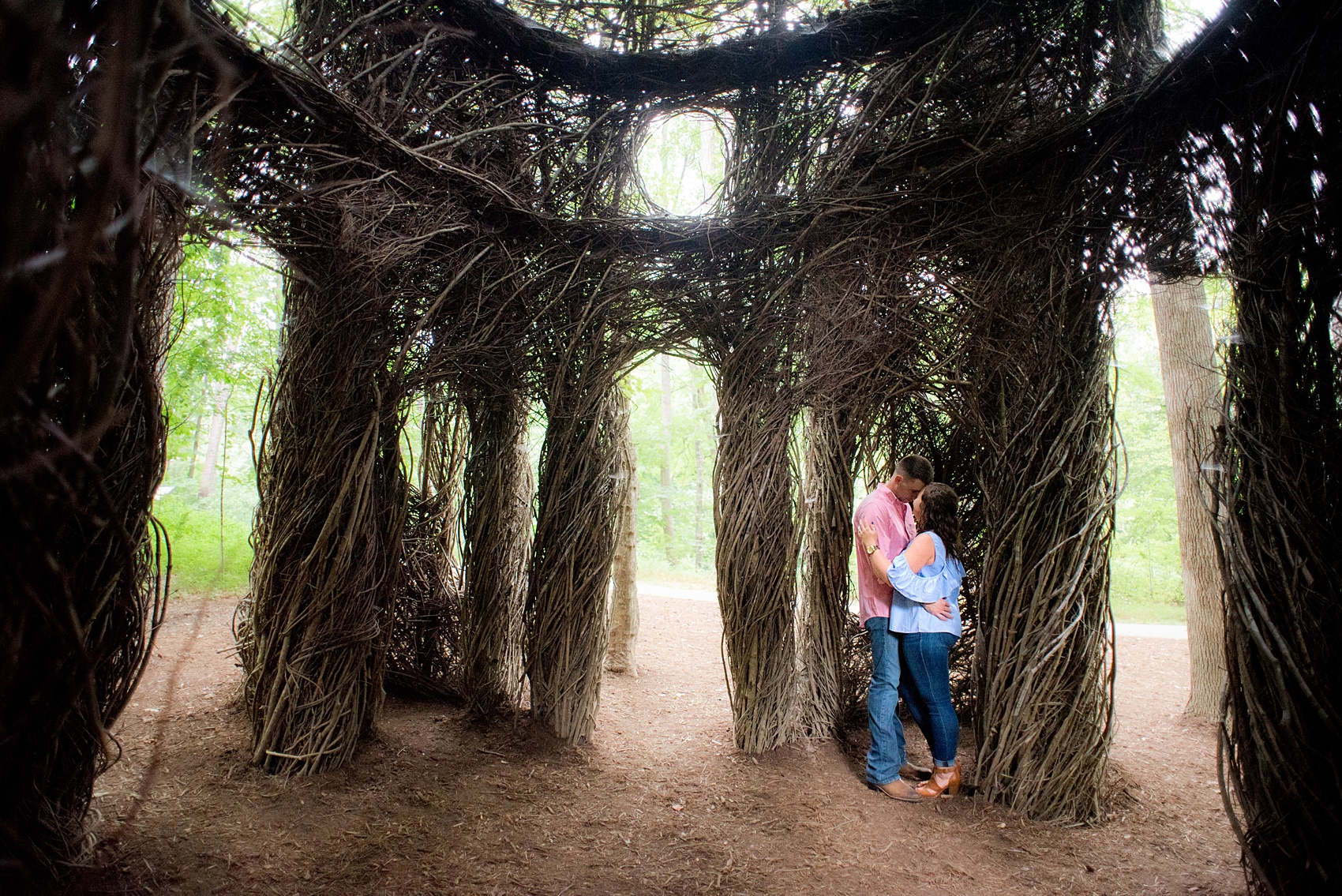 Mikkel Paige Photography photos of an engagement session at Eno Riverwalk in Hillsborough, North Carolina. Picture of bride and groom kissing in a Stick Art sculpture created from branches.