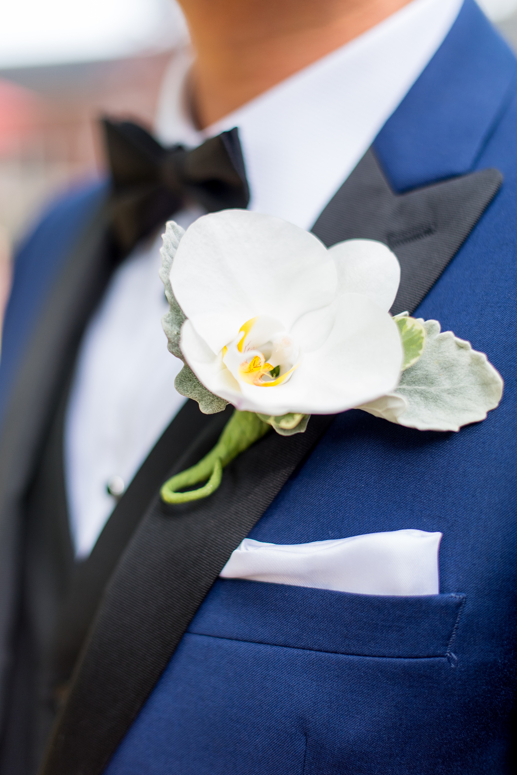 Mikkel Paige Photography pictures of a Westbury Manor wedding on Long Island. Detail photo the groom's white orchid boutonniere on his blue suit with black lapel.