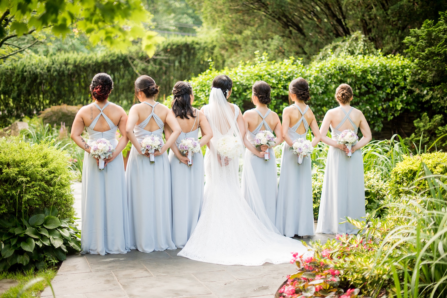 Mikkel Paige Photography pictures of a Westbury Manor wedding on Long Island. Photo of the bridal party in blue-grey gowns with flower bouquets behind their backs.