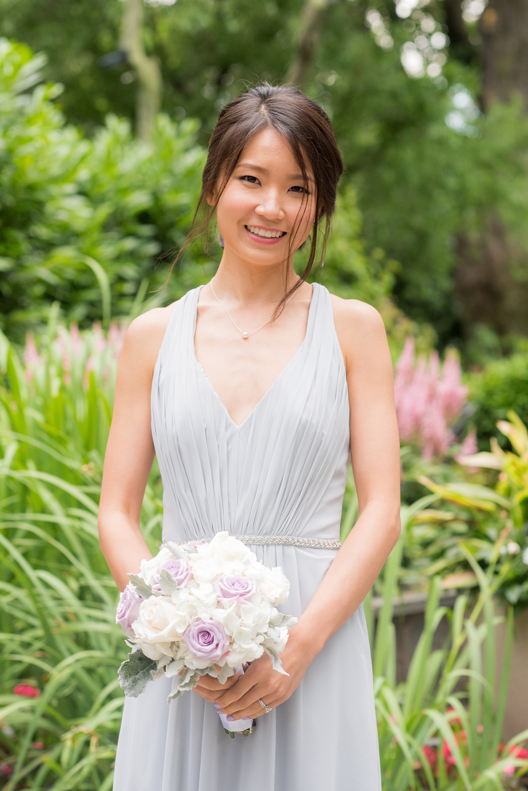 Mikkel Paige Photography pictures of a Westbury Manor wedding on Long Island. Photo of a bridesmaid in a blue-grey gowns with a white and lavender bouquet.