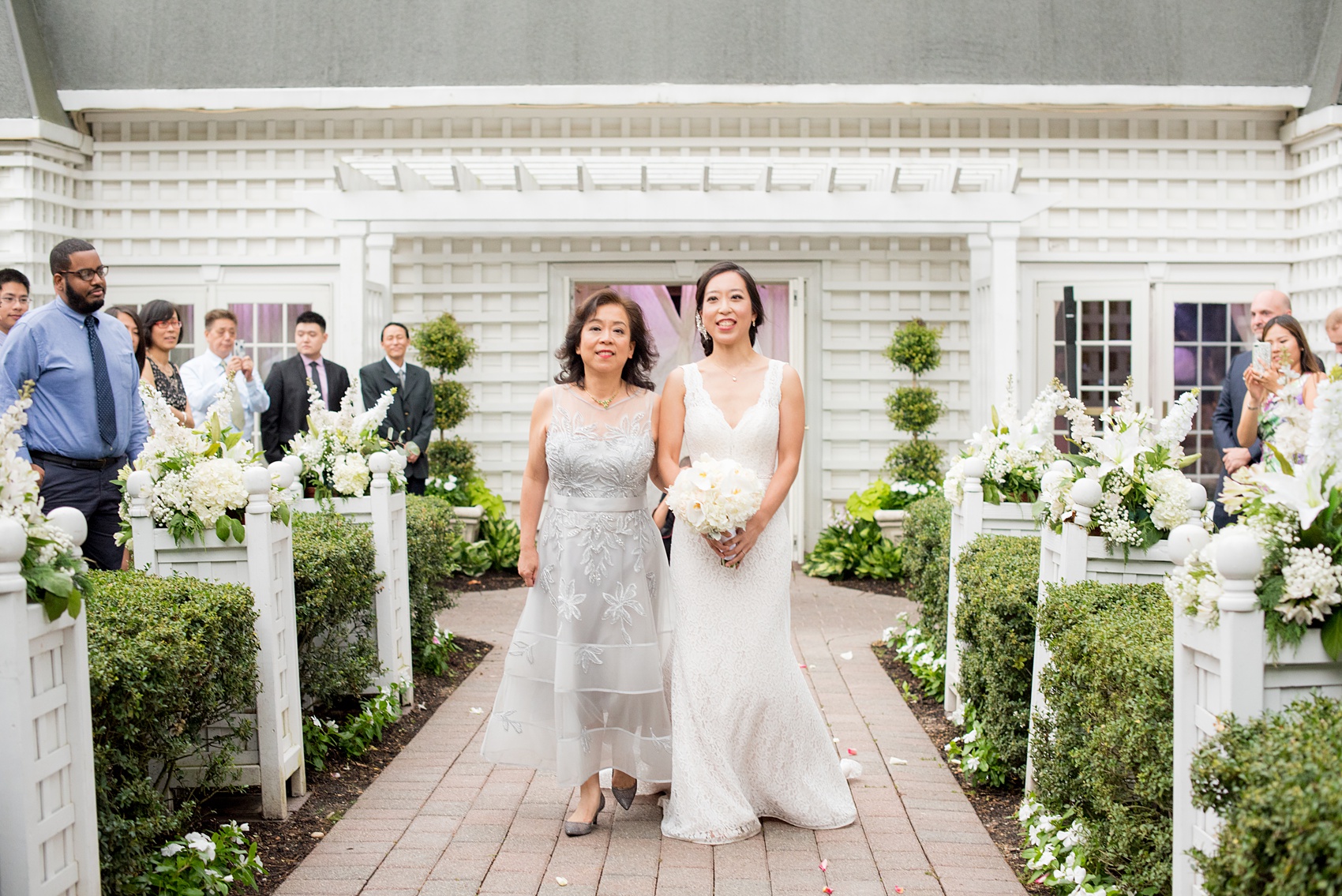 Mikkel Paige Photography pictures of a Westbury Manor wedding on Long Island. Photo of the bride and her mother walking down the aisle at their outdoor ceremony.