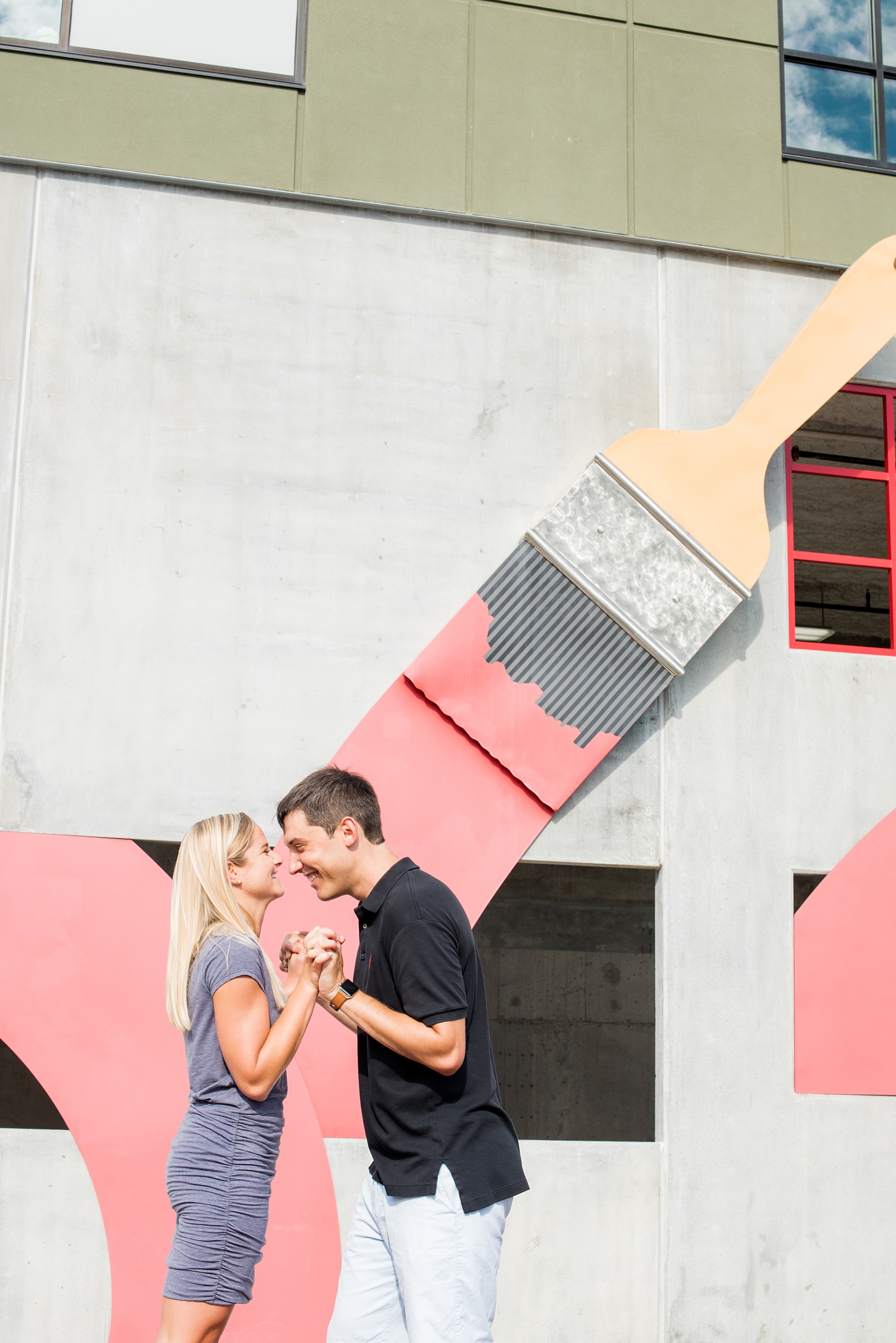 Mikkel Paige Photography pictures of a colorful engagement session in Chapel Hill North Carolina. The bride and groom smile next to a paintbrush wall mural.