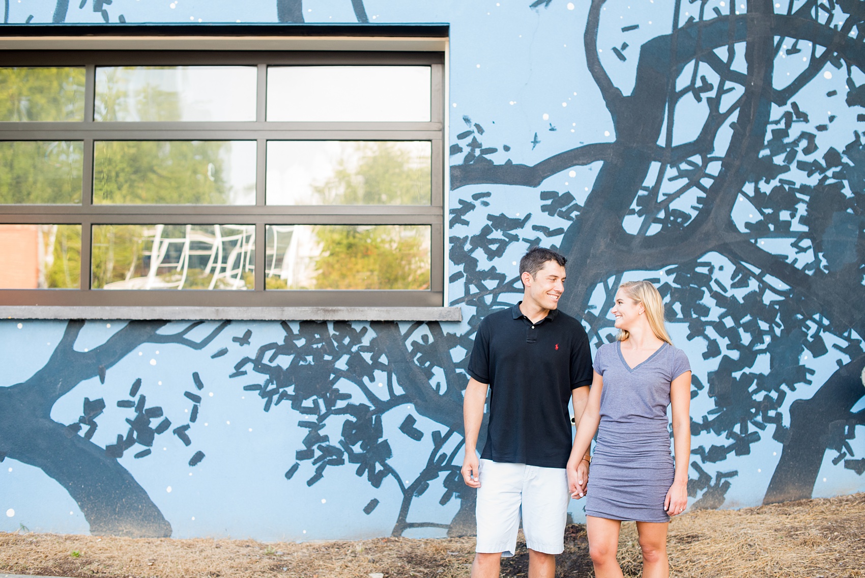 Mikkel Paige Photography pictures of a colorful engagement session in Chapel Hill North Carolina. Image of the bride and groom in front of a black and blue tree silhouette mural.