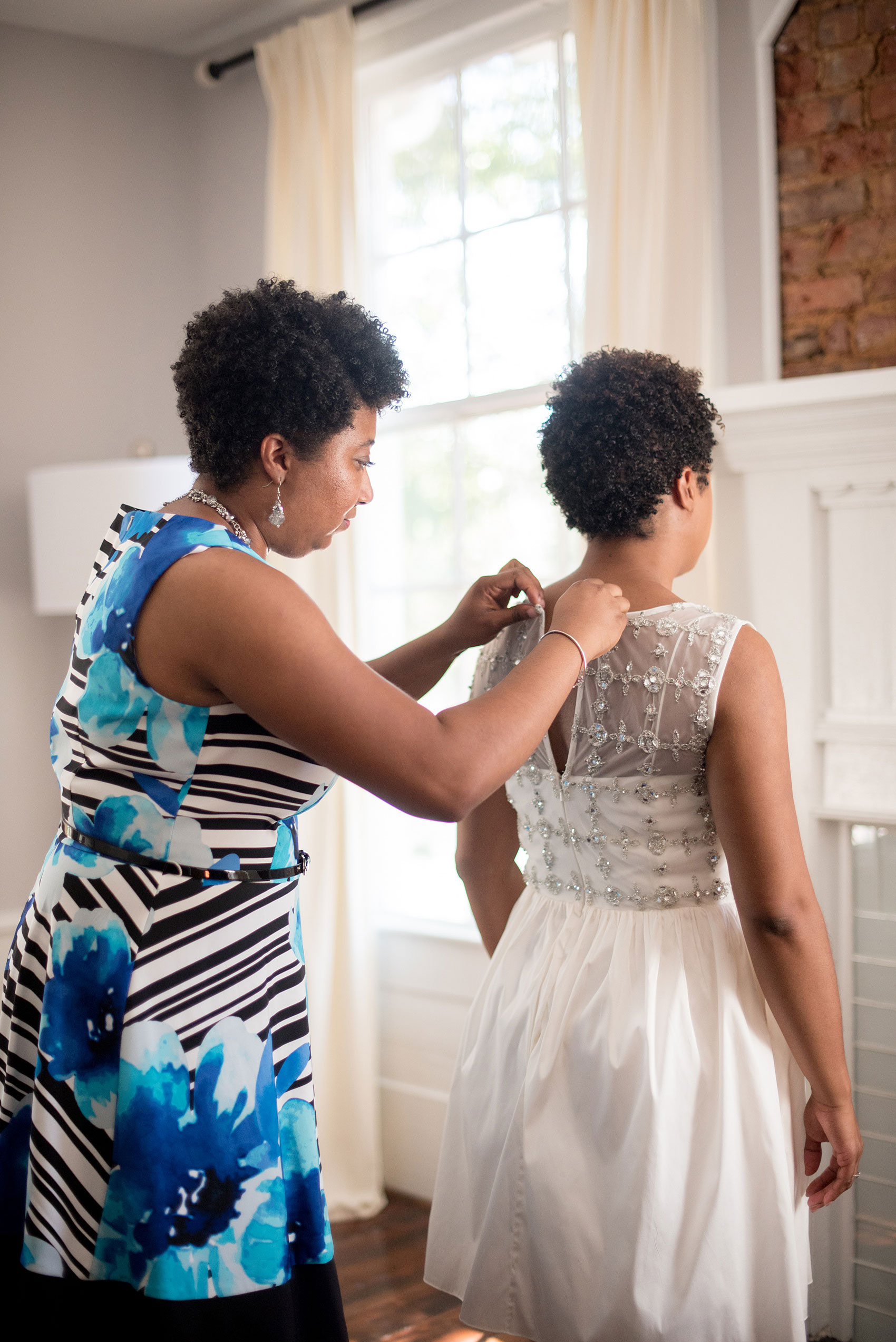 Mikkel Paige Photography pictures of a wedding at Leslie-Alford Mim's House in North Carolina for a Mad Dash Weddings event. Photo of the bride's sister helping her get ready in the bridal suite.