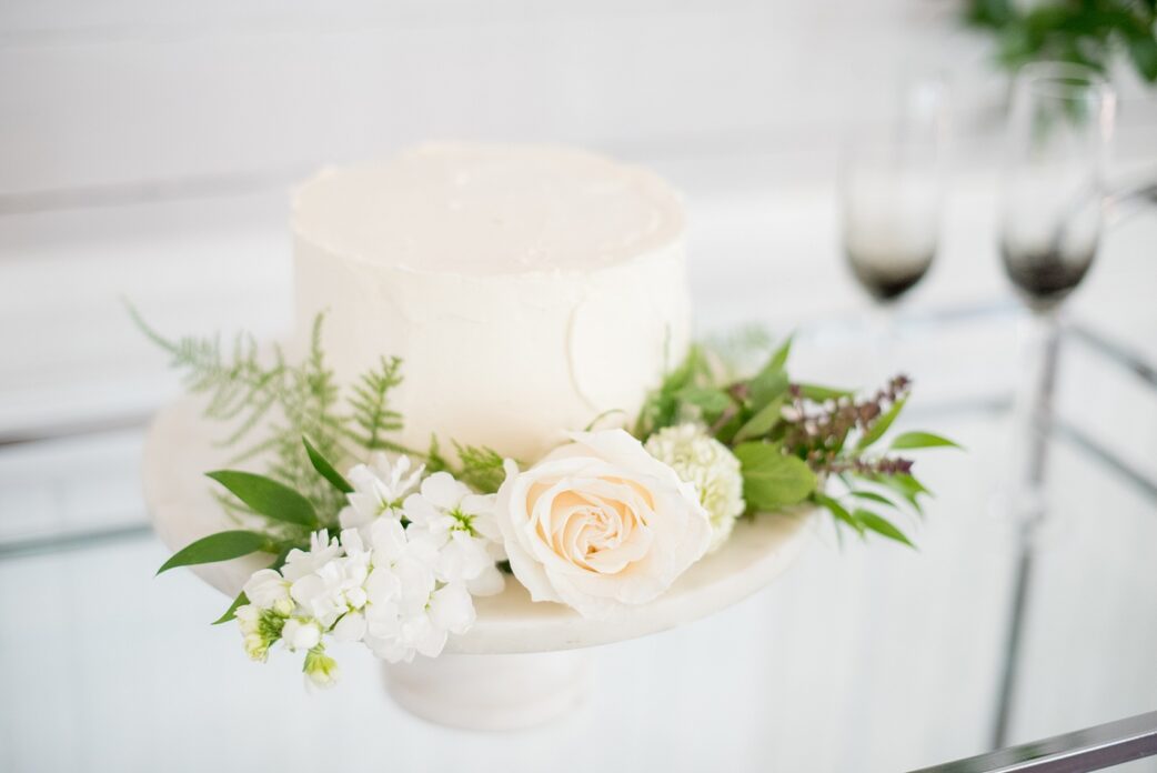 Mikkel Paige Photography pictures of a wedding at Leslie-Alford Mim's House in North Carolina for a Mad Dash Weddings event. Photo of the petite red-velvet, white frosted wedding cake adorned with flowers.