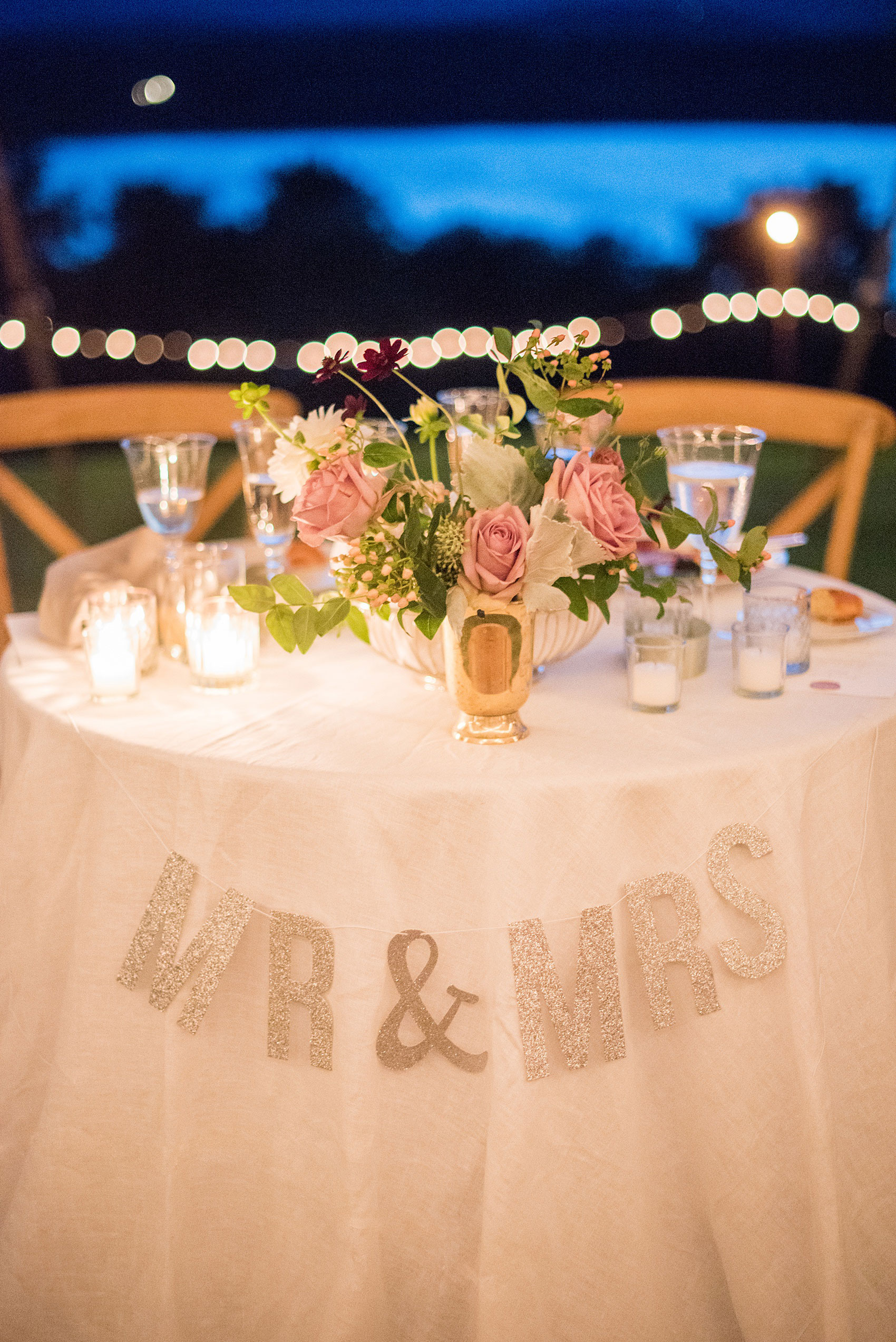 Mikkel Paige Photography photos from a Southwood Estate Wedding in Germantown, New York in the Hudson Valley. Picture of the round sweetheart table with floral centerpiece and silver glitter Mr. and Mrs. sign by candlelight.