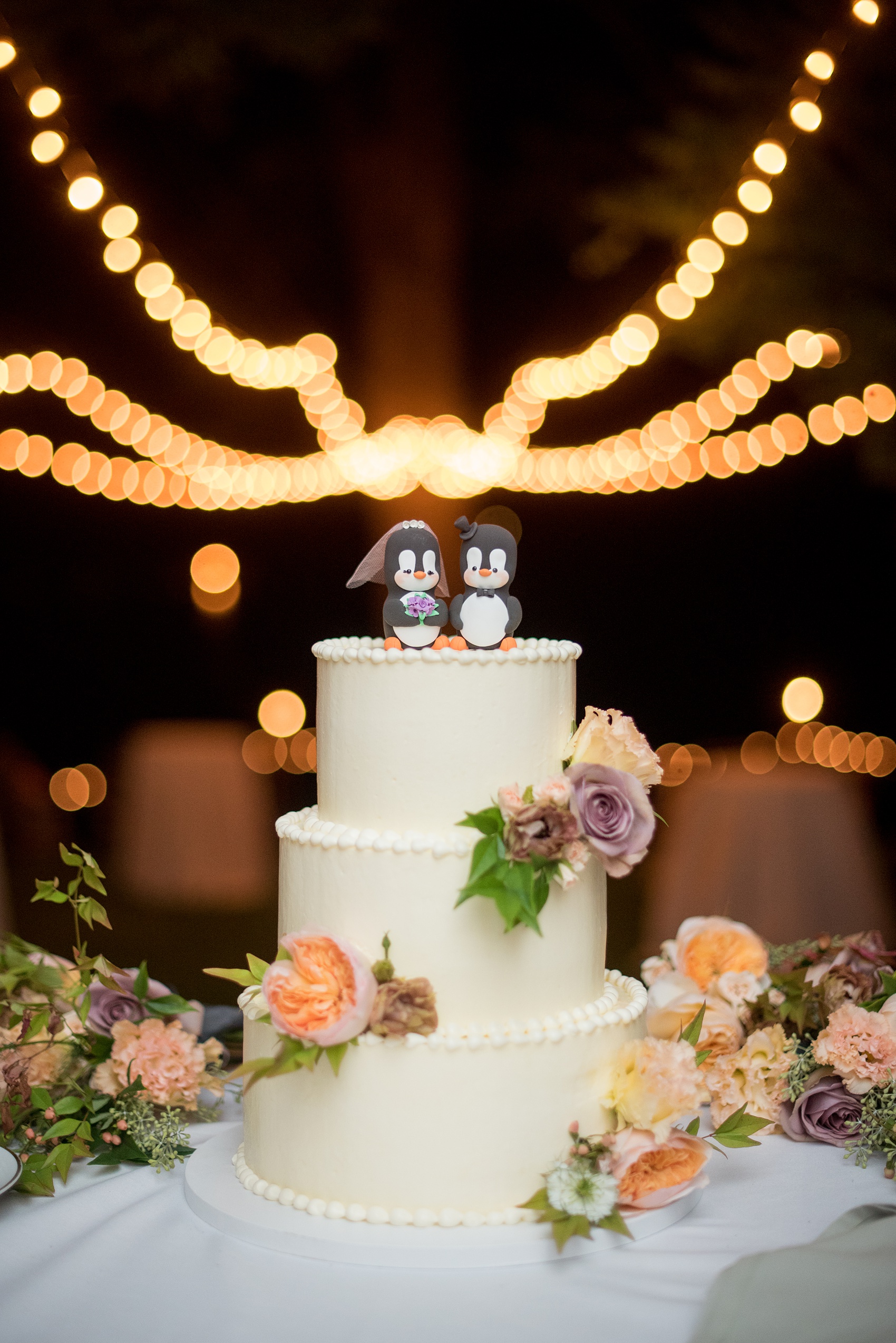 Mikkel Paige Photography photos from a Southwood Estate Wedding in Germantown, New York in the Hudson Valley. Picture of the white buttercream cake with penguin cake topper decorated with flowers.