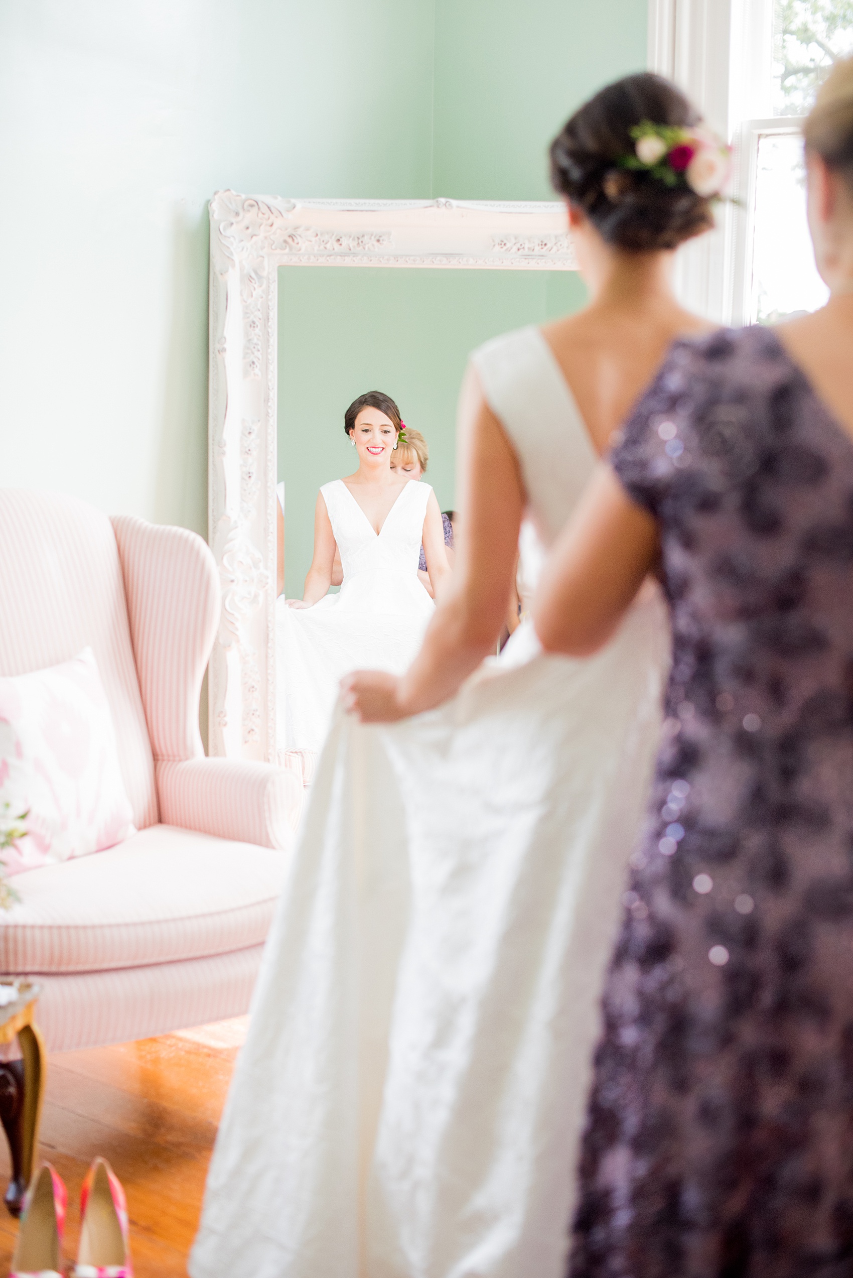 Mikkel Paige Photography pictures from a wedding at Merrimon-Wynne House in Raleigh, NC. Photo of the bride reflecting in a mirror in the bridal suite as her mother helps her get ready.