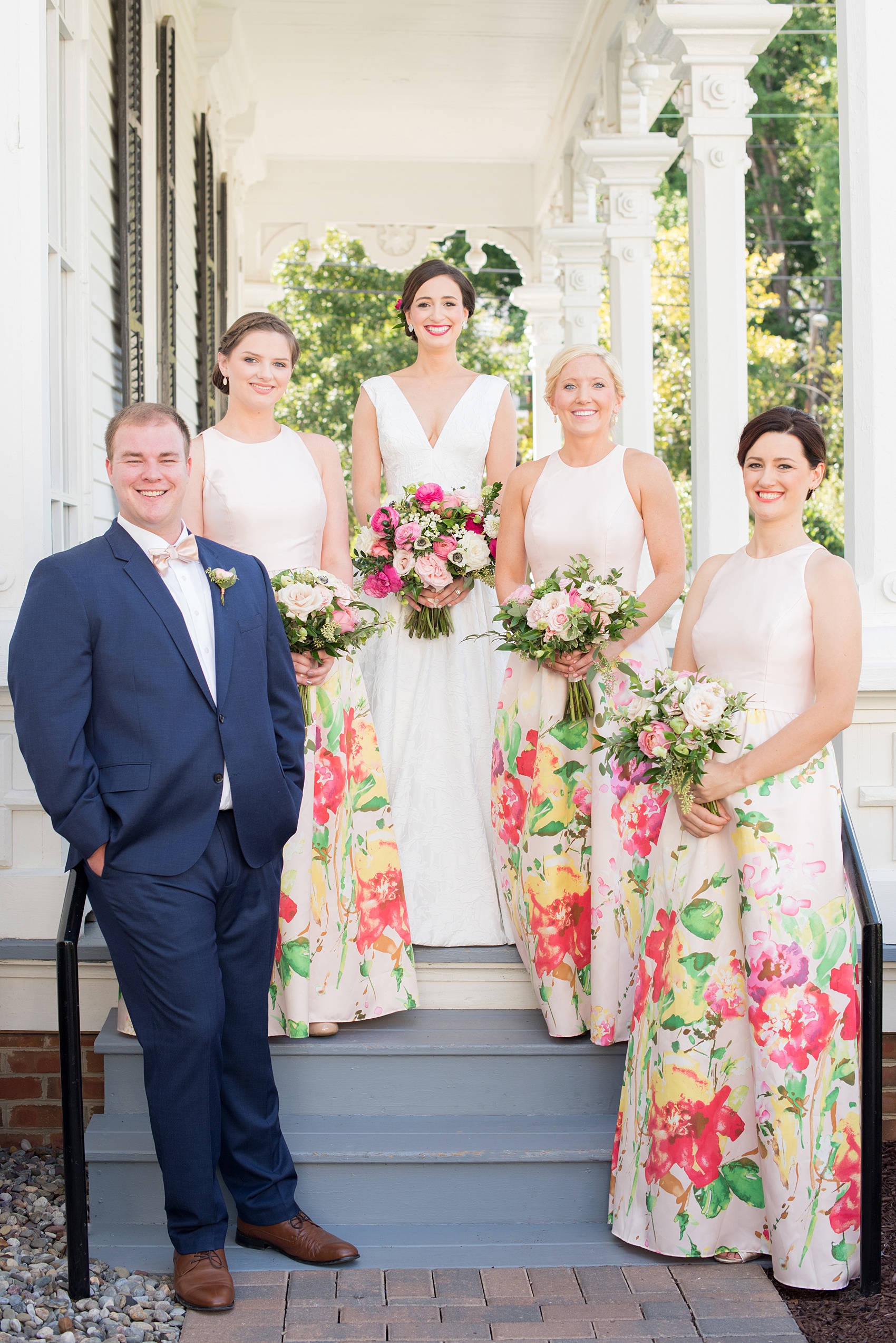 Mikkel Paige Photography pictures from a wedding at Merrimon-Wynne House in Raleigh, NC. Photo of the bridal party on the porch of the historic home. The bridesmaids wore pink dresses with a colorful floral pattern.