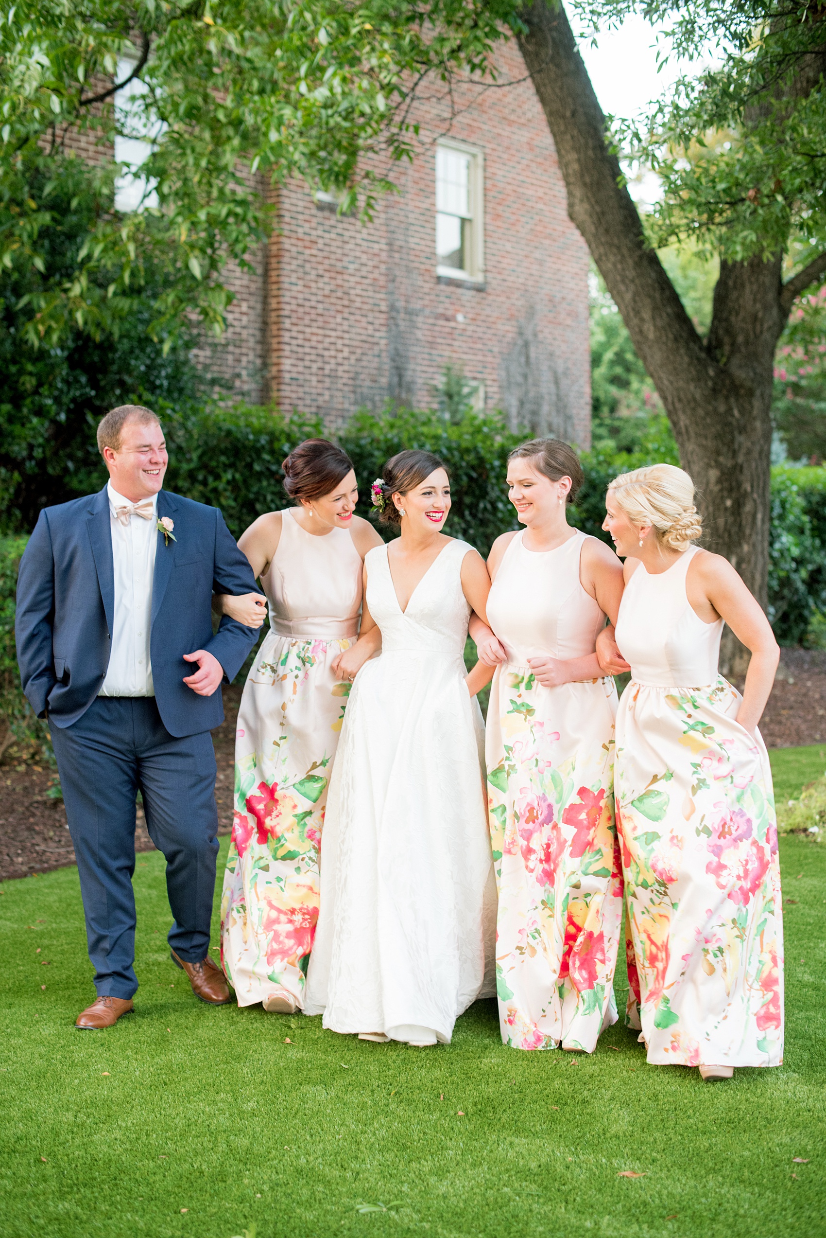 Mikkel Paige Photography pictures from a wedding at Merrimon-Wynne House in Raleigh, NC. Photo of the bride walking with her bridal party and pattern floral pink dresses.