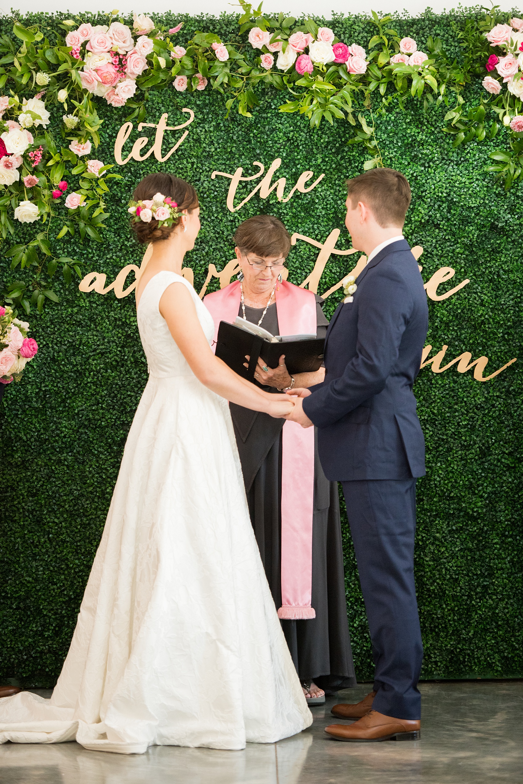 Mikkel Paige Photography pictures from a wedding at Merrimon-Wynne House in Raleigh, NC. Photo of the ceremony with boxwood greenery backdrop with pink roses and script wood gold letters.