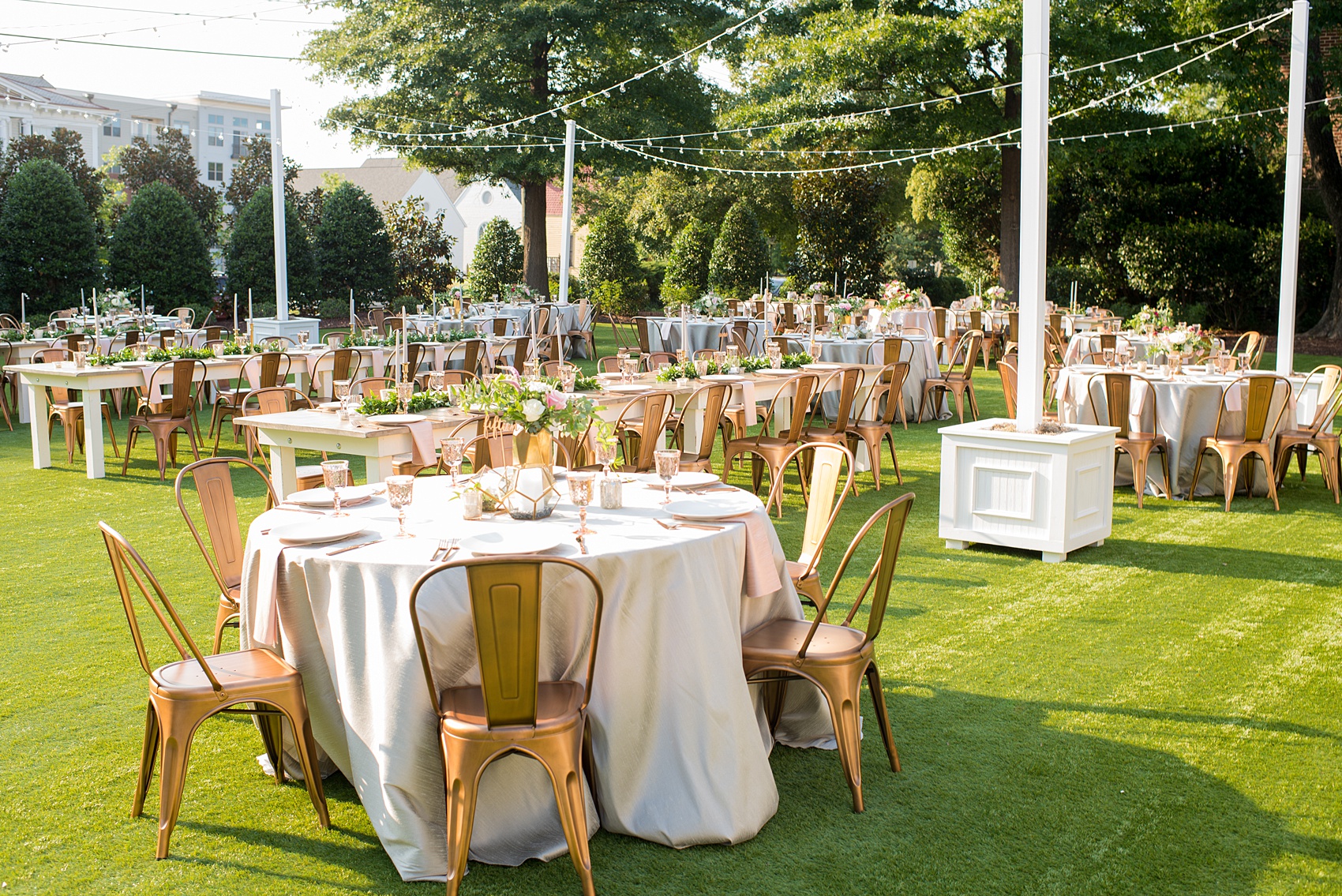 Mikkel Paige Photography pictures from a wedding at Merrimon-Wynne House in Raleigh, NC. Photo of the outdoor reception on the lawn, with round and rectangular farm tables, pink linen napkins, grey plates, and floral centerpieces.
