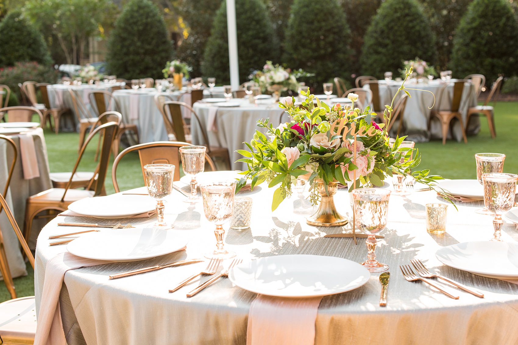 Mikkel Paige Photography pictures from a wedding at Merrimon-Wynne House in Raleigh, NC. Photo of the table centerpieces with geometric glass candle holders, script gold numbers, copper flatware, and pink glasses.