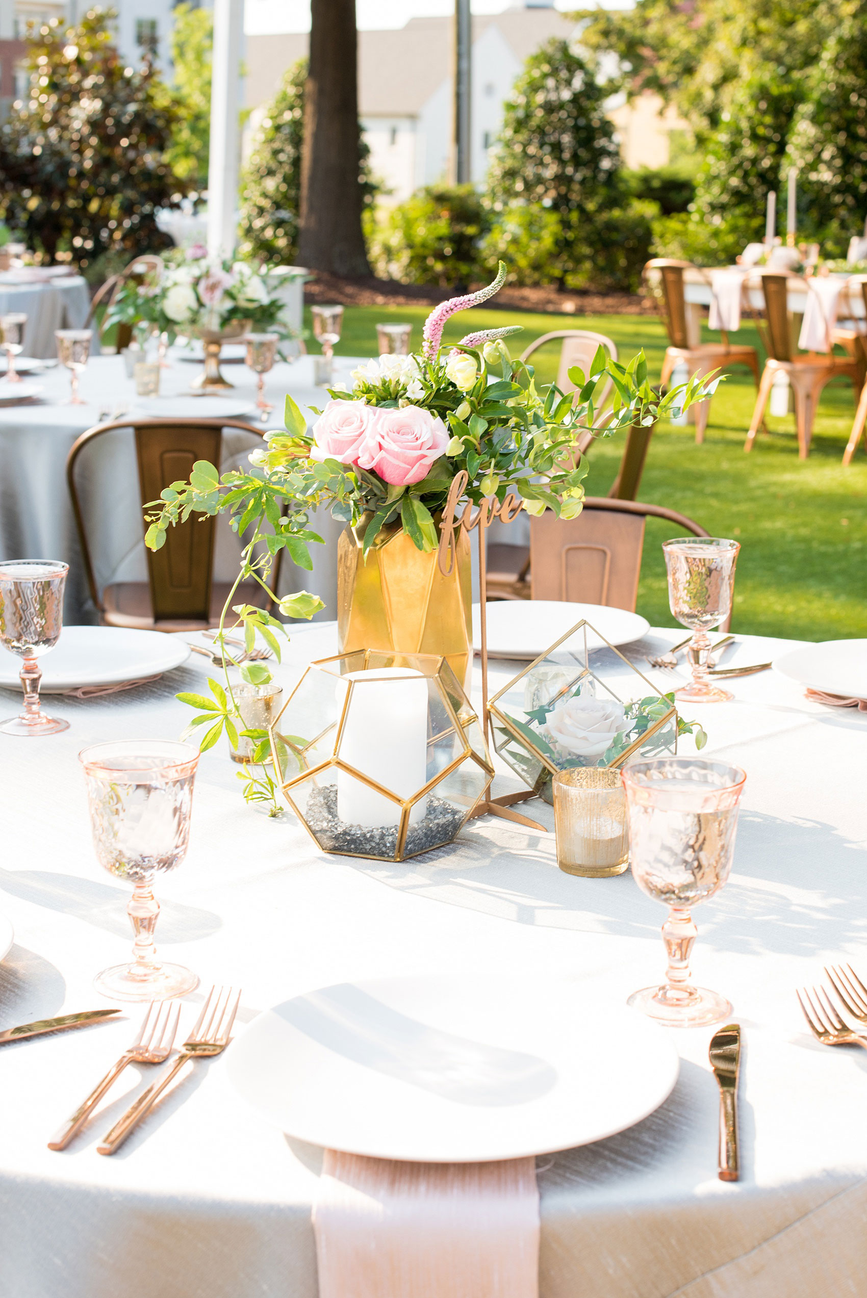 Mikkel Paige Photography pictures from a wedding at Merrimon-Wynne House in Raleigh, NC. Photo of the table centerpieces with geometric glass candle holders, script gold numbers, and pink glasses.