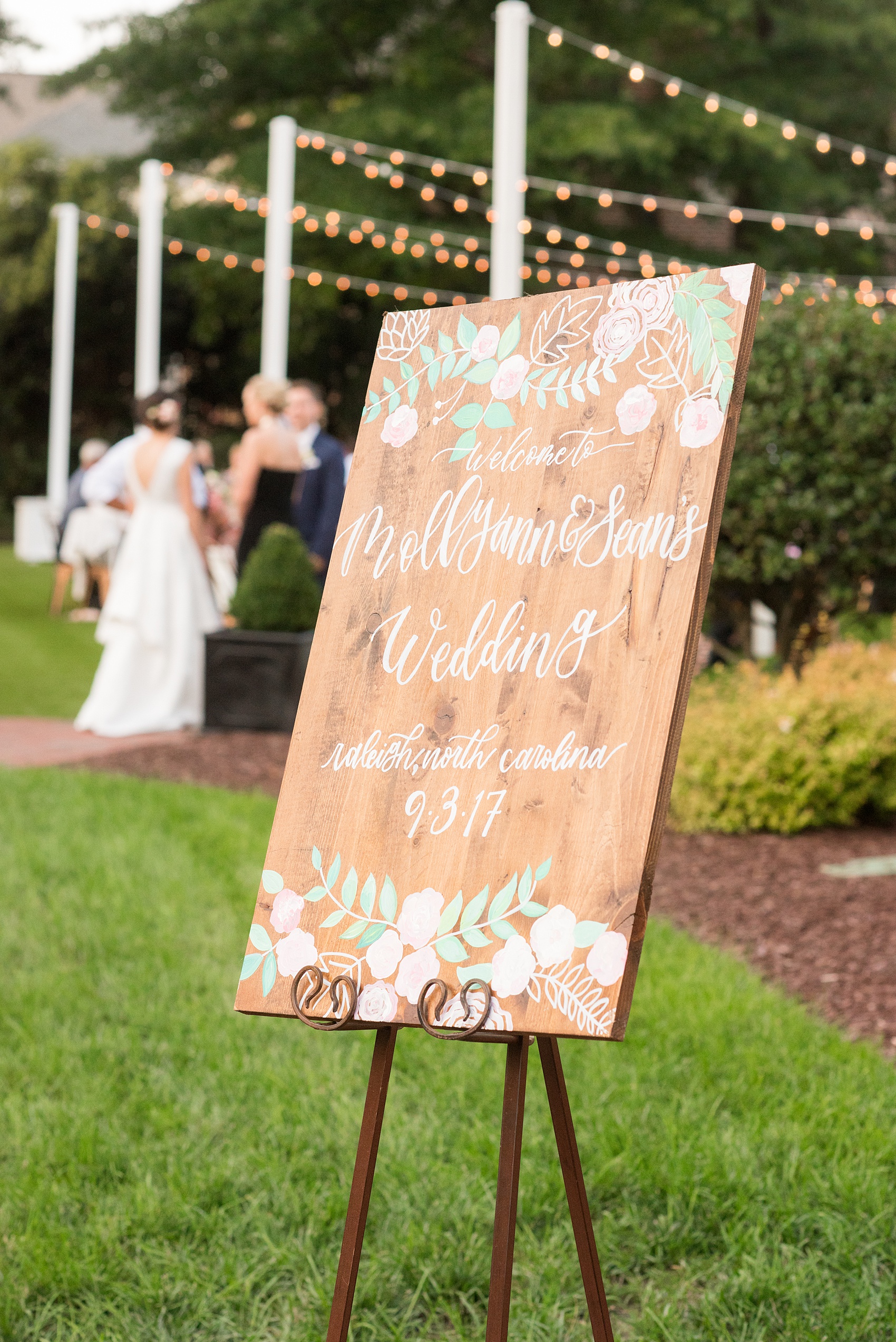 Mikkel Paige Photography pictures from a wedding at Merrimon-Wynne House in Raleigh, NC. Photo of the bride and groom's custom white script sign on wood, painted with pink and green flowers.