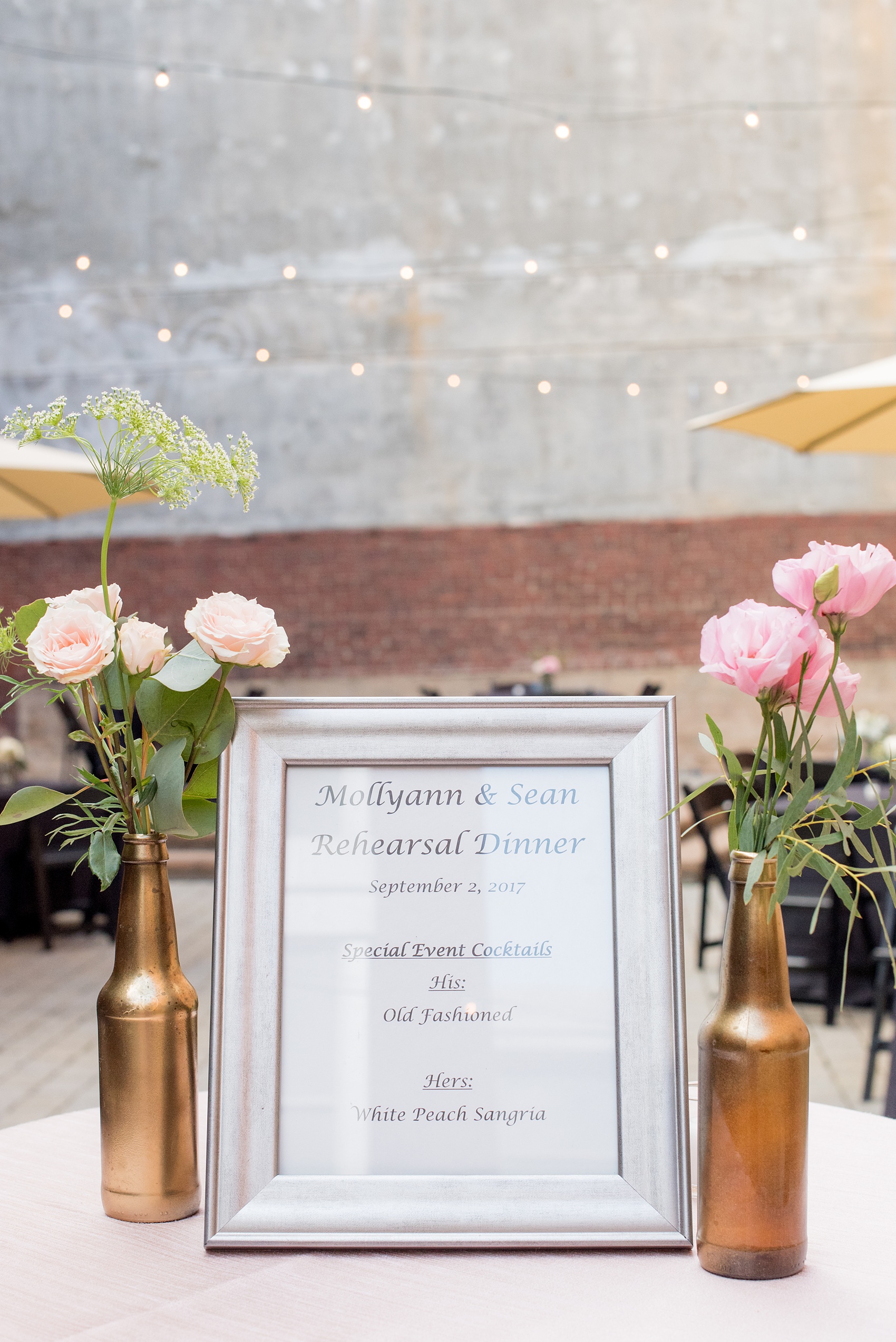 Mikkel Paige Photography photos from a downtown Raleigh wedding rehearsal dinner at Sitti restaurant. Picture of the specialty cocktail menu with gold spray painted bottles and flowers next to it.