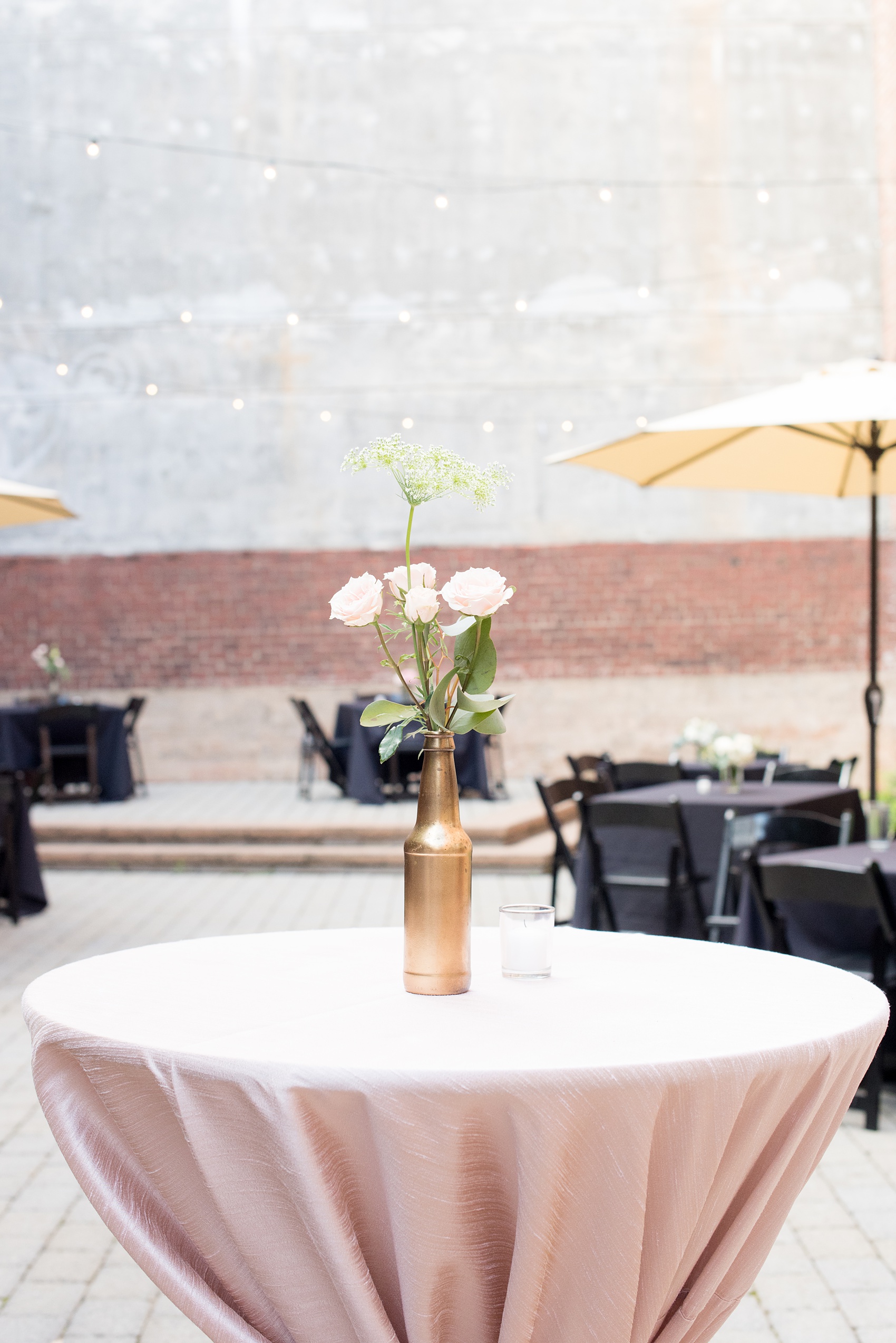 Mikkel Paige Photography photos from a downtown Raleigh wedding rehearsal dinner at Sitti restaurant. Picture of the pink hightop tables with pink linens and gold wraps. Centerpieces with gold bottles and flowers were on top of the tables.