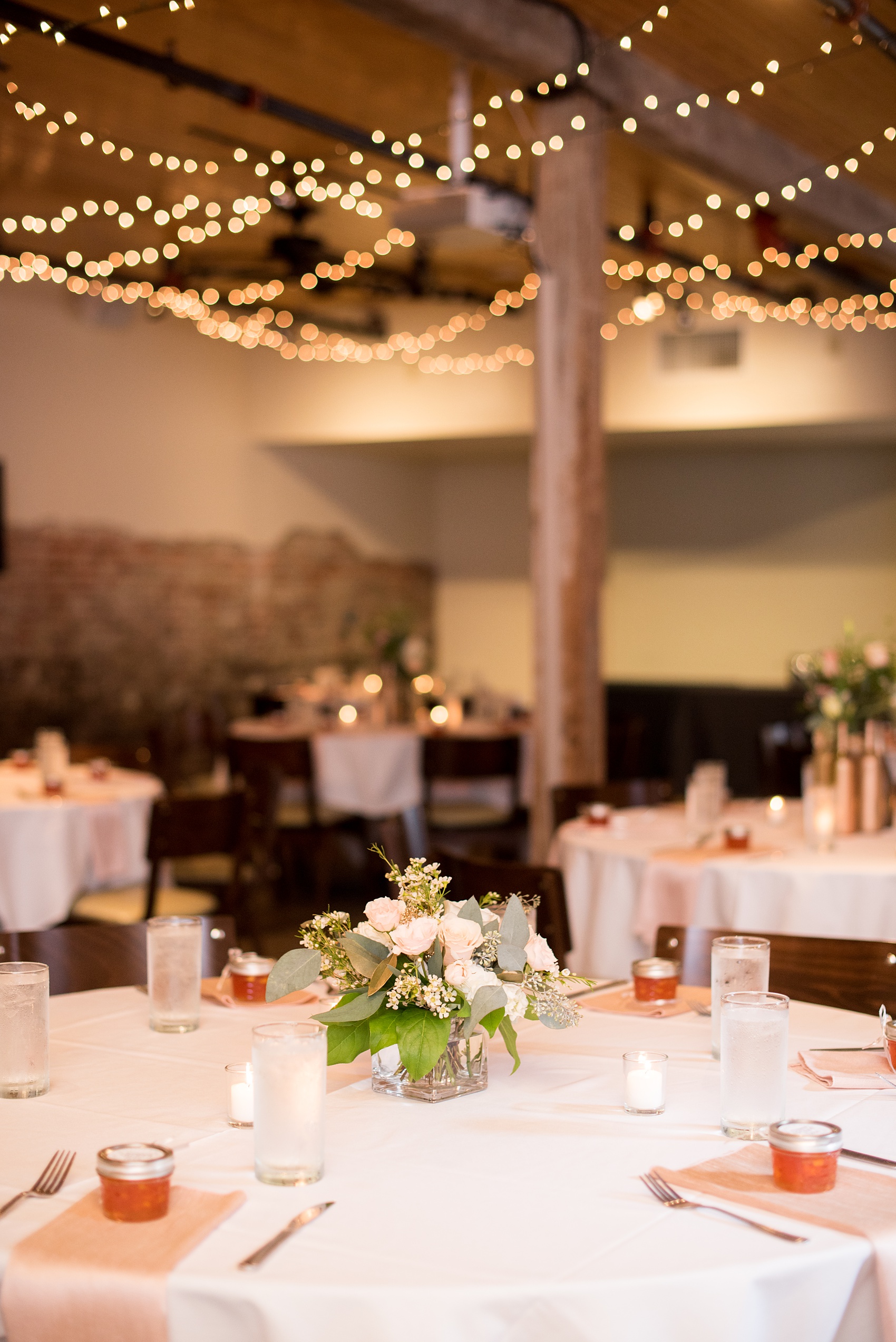 Mikkel Paige Photography photos from a downtown Raleigh wedding rehearsal dinner at Sitti restaurant. Photo of the inside seated dinner with candlelight, twinkle lights, floral centerpieces and jam guest favors.