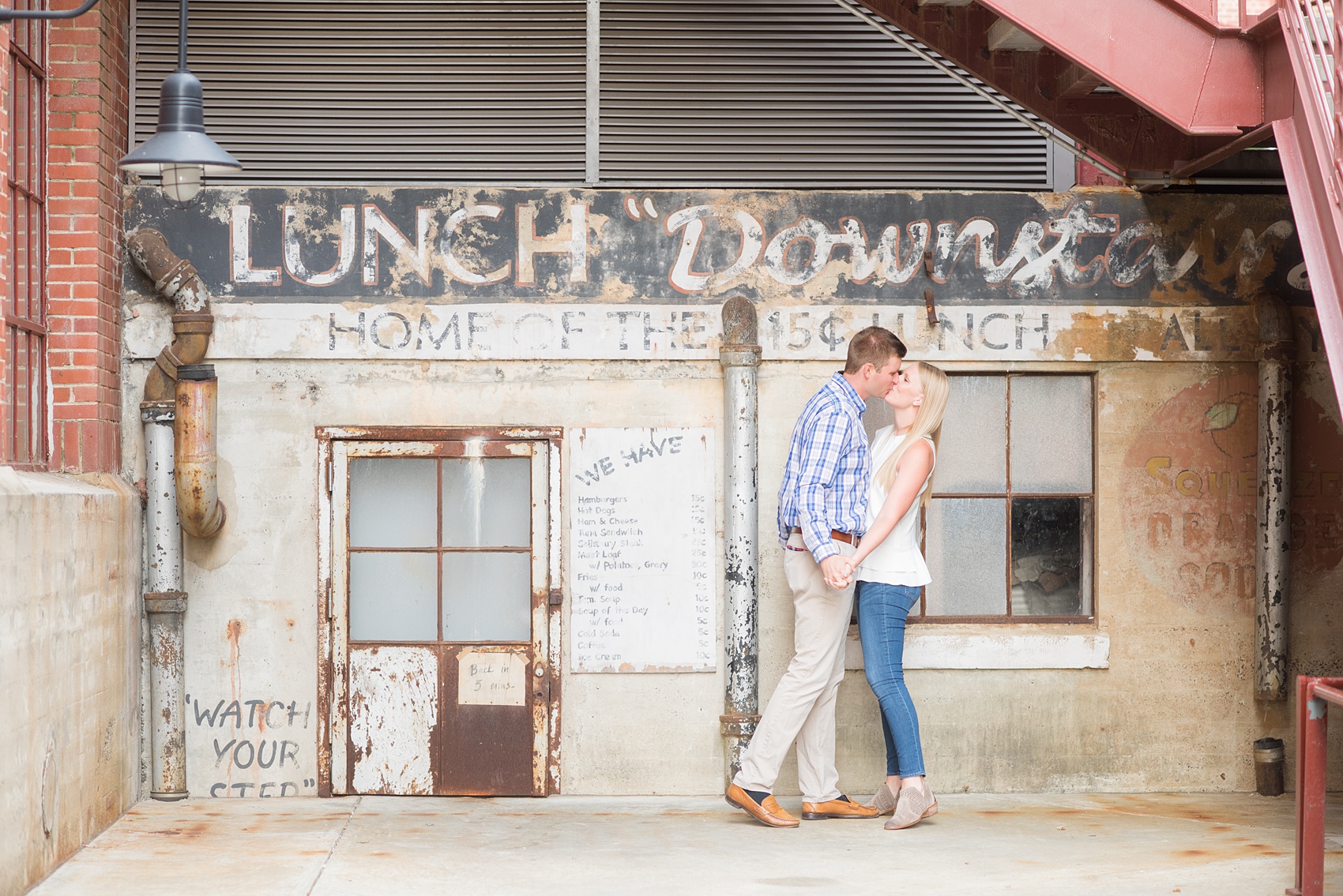 Mikkel Paige Photography photos from an engagement session at Durham's American Tobacco Campus in North Carolina. Picture of the couple near vintage signage.