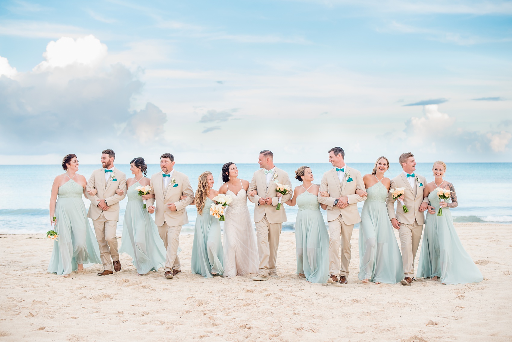 Mikkel Paige Photography photos from a wedding at Grand Paraiso, Mexico, Playa del Carmen Iberostar resort. Picture of the bridal party in mint green gowns and groomsmen in tan suits walking on the beach.