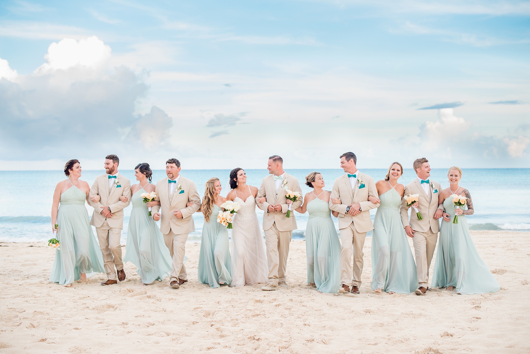 Mikkel Paige Photography photos from a wedding at Grand Paraiso, Mexico, Playa del Carmen Iberostar resort. Picture of the bridal party in mint green gowns and groomsmen in tan suits walking on the beach.