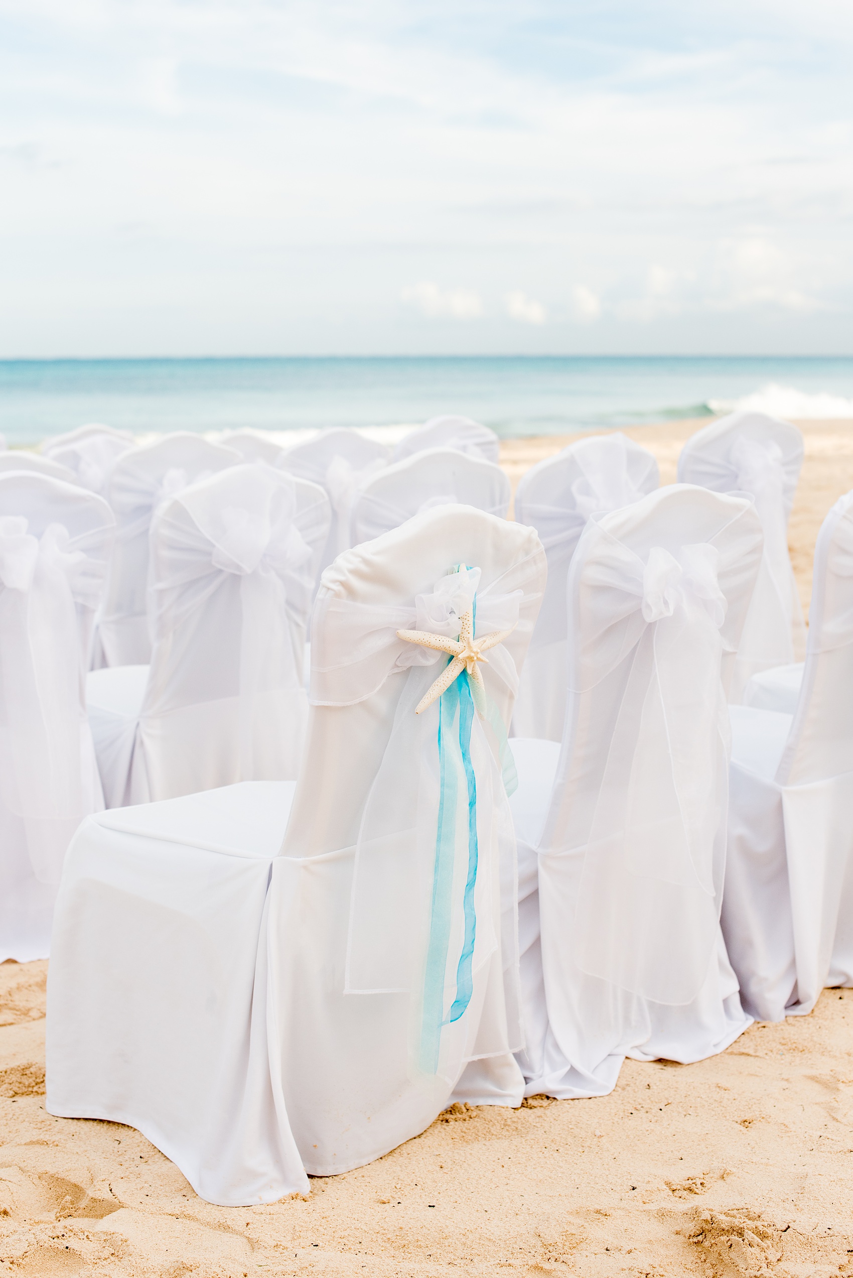 Mikkel Paige Photography photos from a wedding at Grand Paraiso, Mexico, Playa del Carmen Iberostar resort. Picture of the white chairs for the beach ceremony with a starfish and ribbon detail.