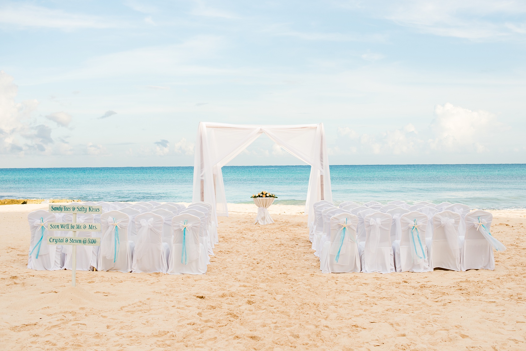 Mikkel Paige Photography photos from a wedding at Grand Paraiso, Mexico, Playa del Carmen Iberostar resort. Picture of the white chairs and fabric arbor for the beach ceremony.