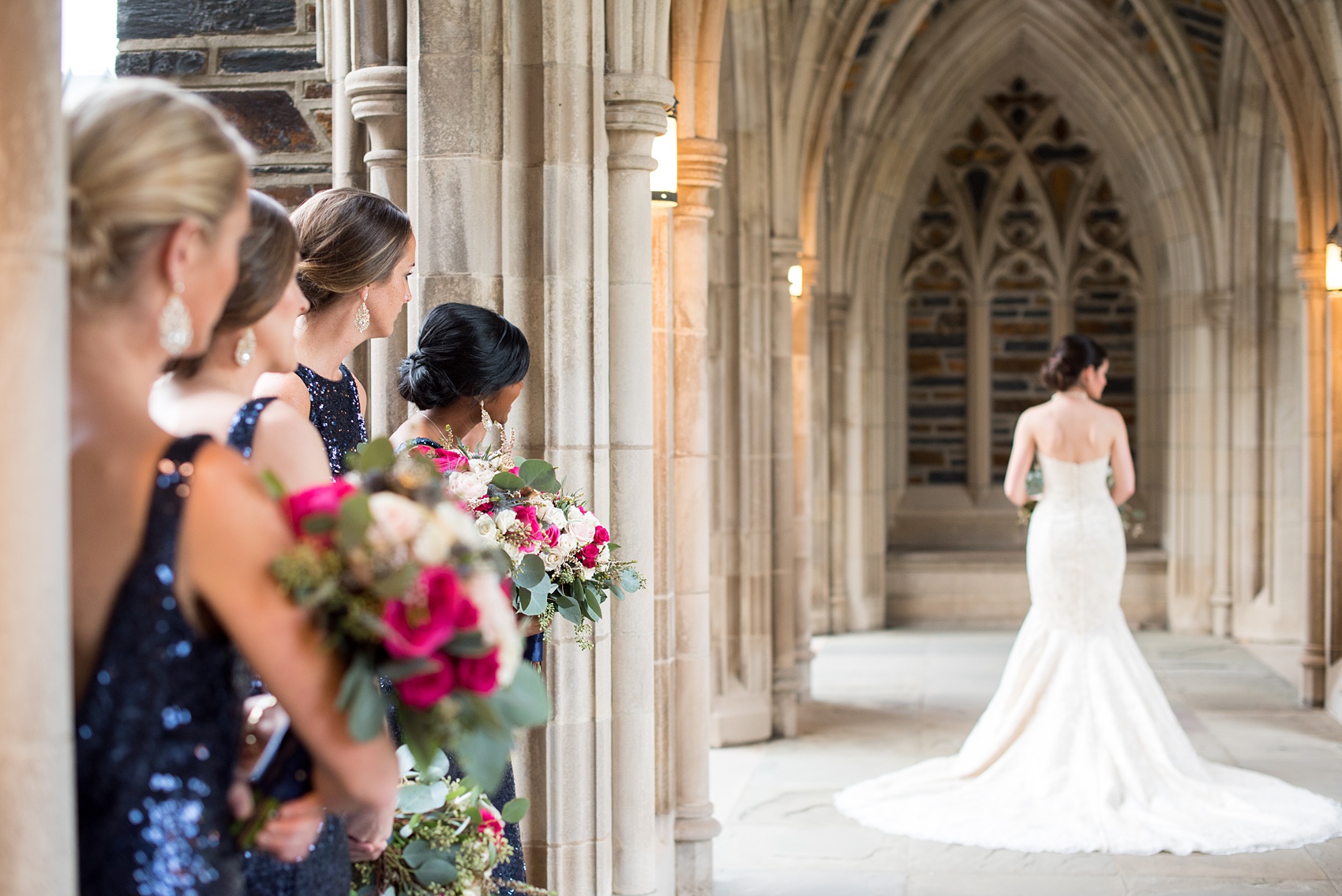 Mikkel Paige Photography photo of a wedding in Chapel Hill at Duke Chapel. Bride and groom with the gothic architecture. A portrait picture of the bride in the gothic arches of the church with her bridesmaids looking on.