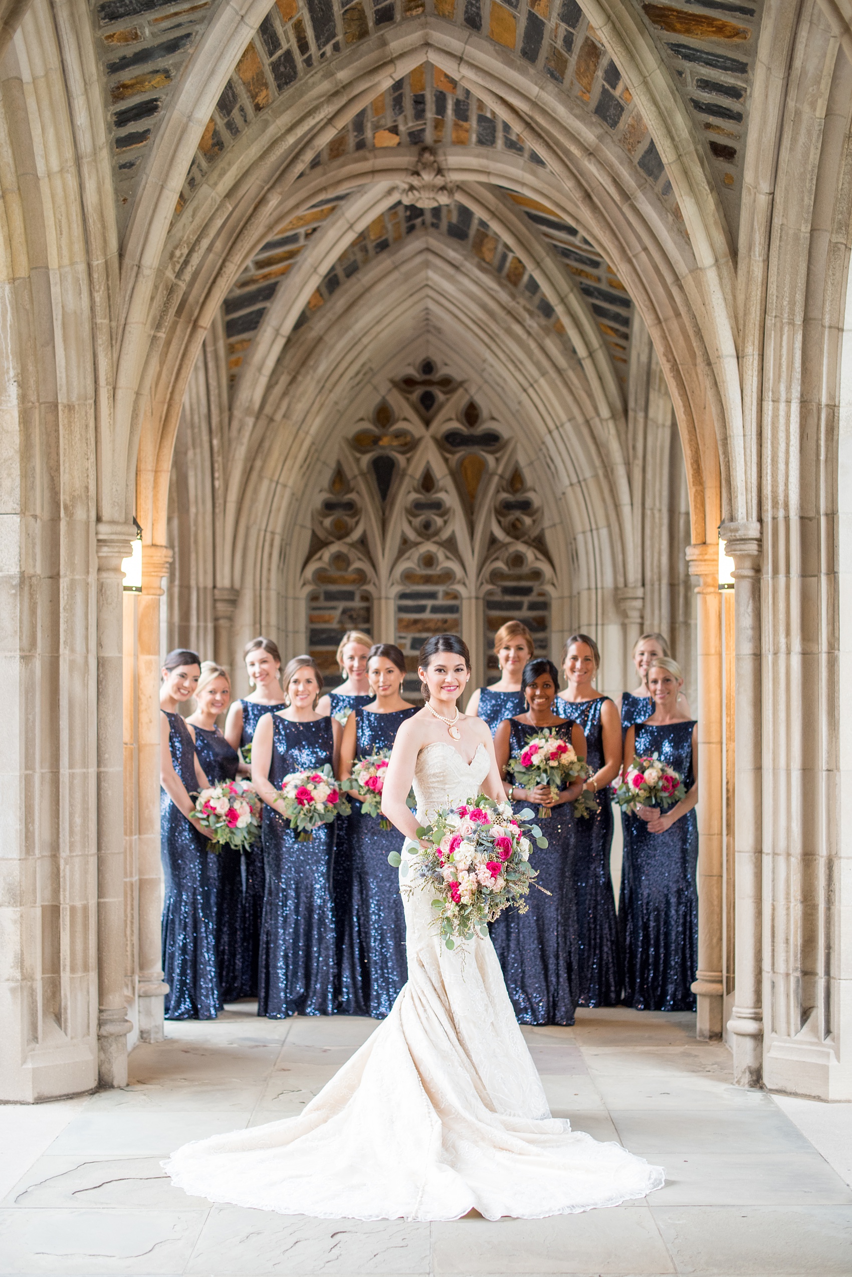 Mikkel Paige Photography photo of a wedding in Chapel Hill at Duke Chapel. Picture of the bridal party in navy blue sequins gowns and the bride in a portrait under the gothic arcade of the church.