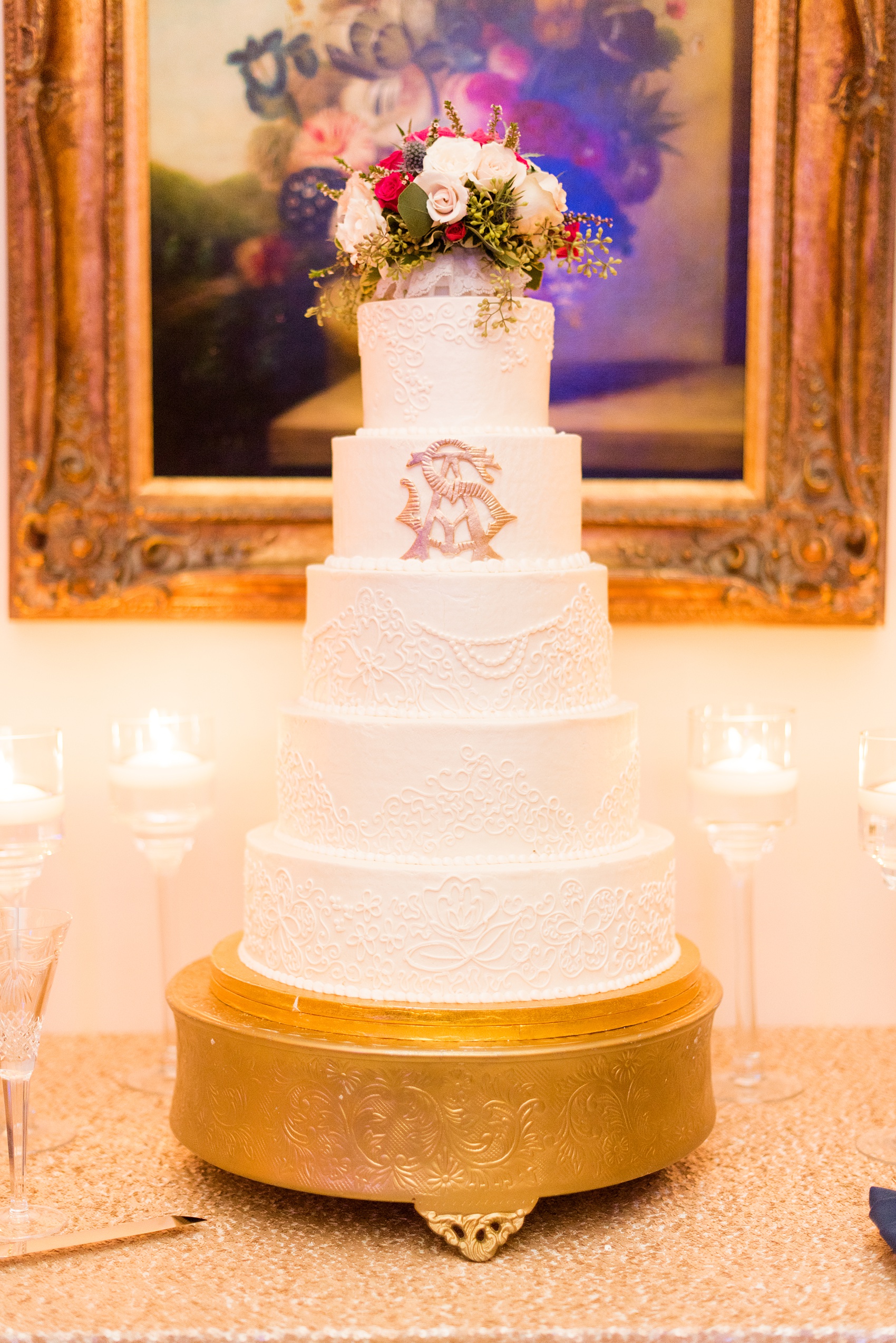 Mikkel Paige Photography photo of a wedding reception at Hope Valley Country Club in Chapel Hill, NC. Picture of the 5 tiered white cake topped with flowers and decorated with a gold monogram.