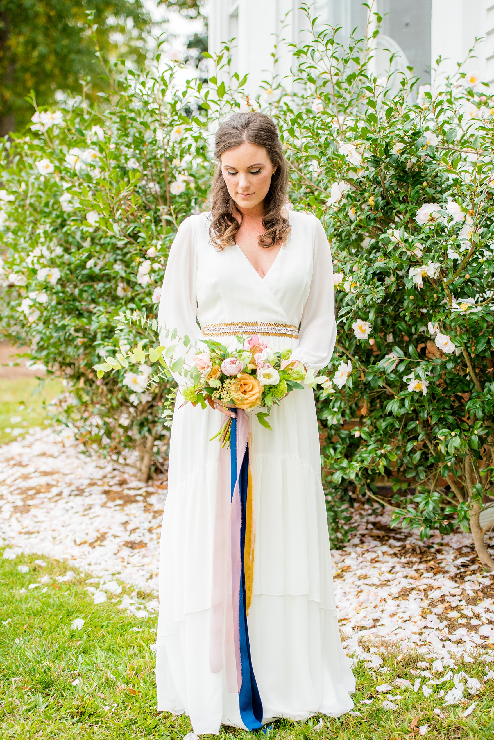 Mikkel Paige Photography photos from a wedding at Leslie-Alford Mims House in North Carolina. Portrait of the bride in her long-sleeve, white chiffon gown from BHLDN and fall flowers with long, autumn ribbons by Caroline Ruth Designs for a Mad Dash Wedding. Pink Camellia flower petals provided the perfect backdrop!