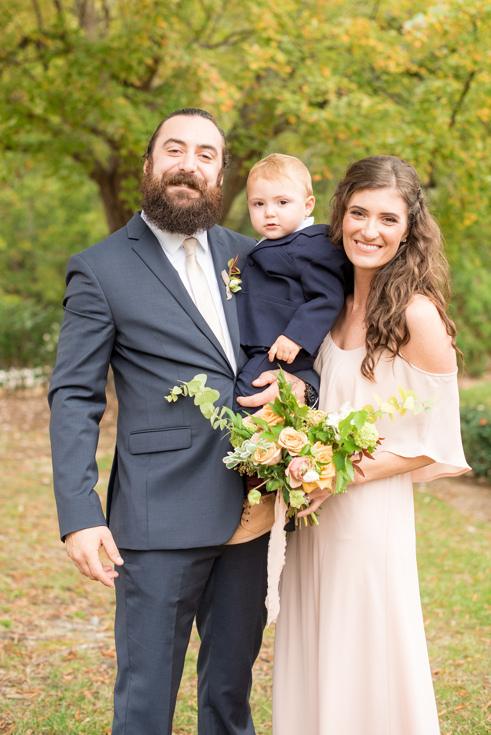 Mikkel Paige Photography photos from a wedding at Leslie-Alford Mims House in North Carolina. Picture of a groomsmen and bridesmaids, with their ring bearer toddler son, in navy linen suits and light pink gown.