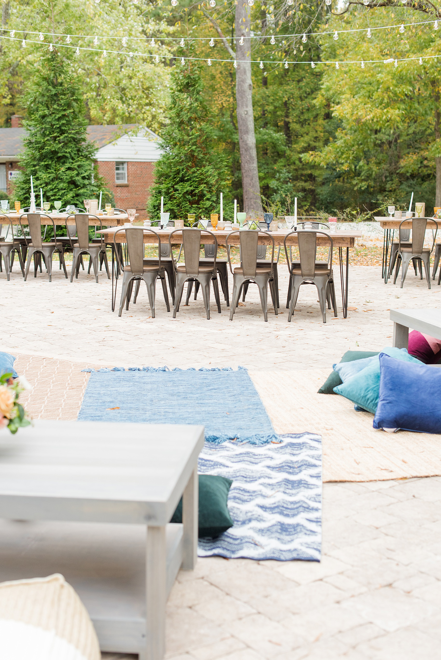 Mikkel Paige Photography photos from a wedding at Leslie-Alford Mims House in North Carolina. Picture of the outdoor reception setup with farm tables, metal chairs and rugs and pillow seating.