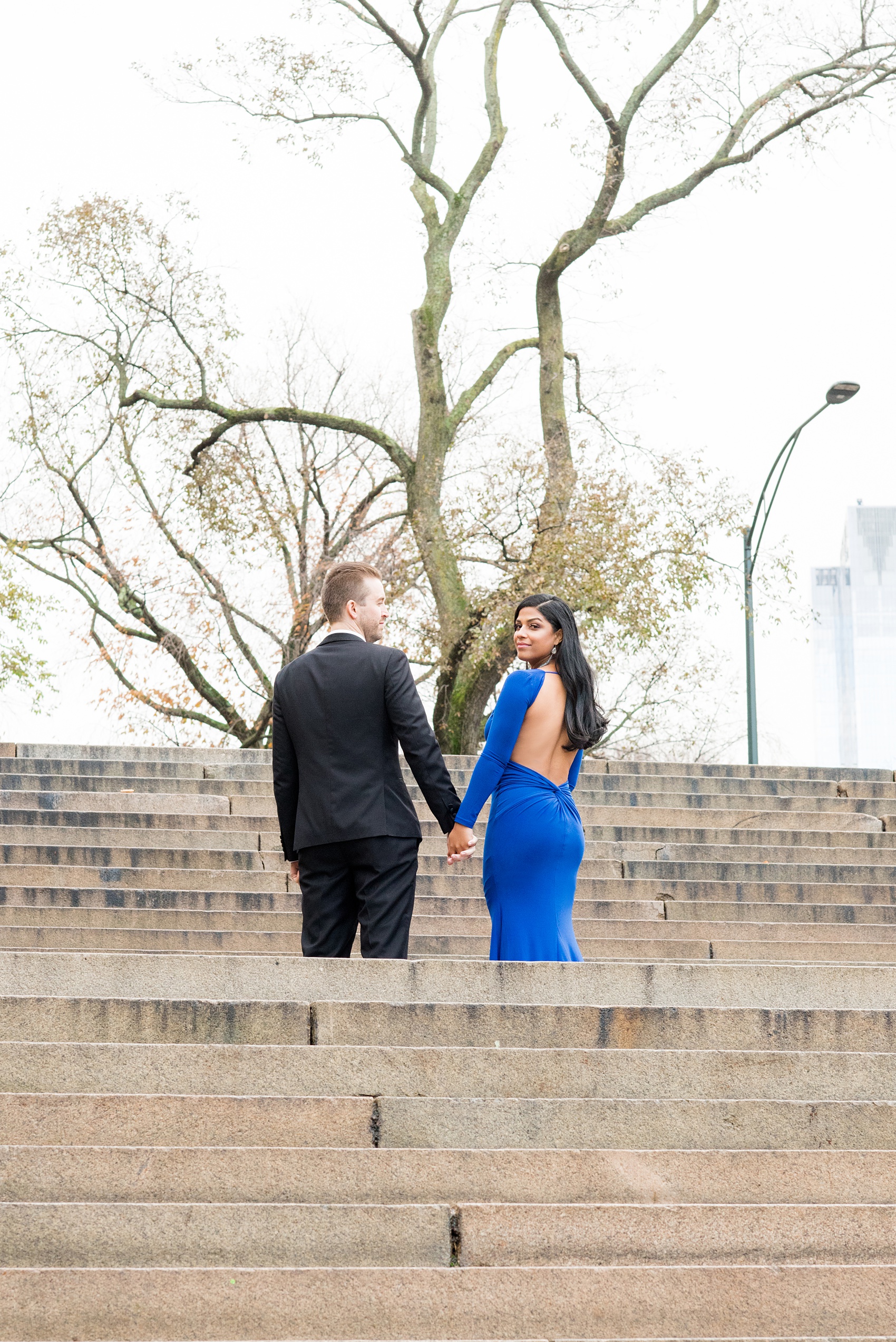 Mikkel Paige Photography pictures of an engagement session in Central Park. A photo of the bride and groom in formal attire walking up the stairs of Bethesda Terrace.