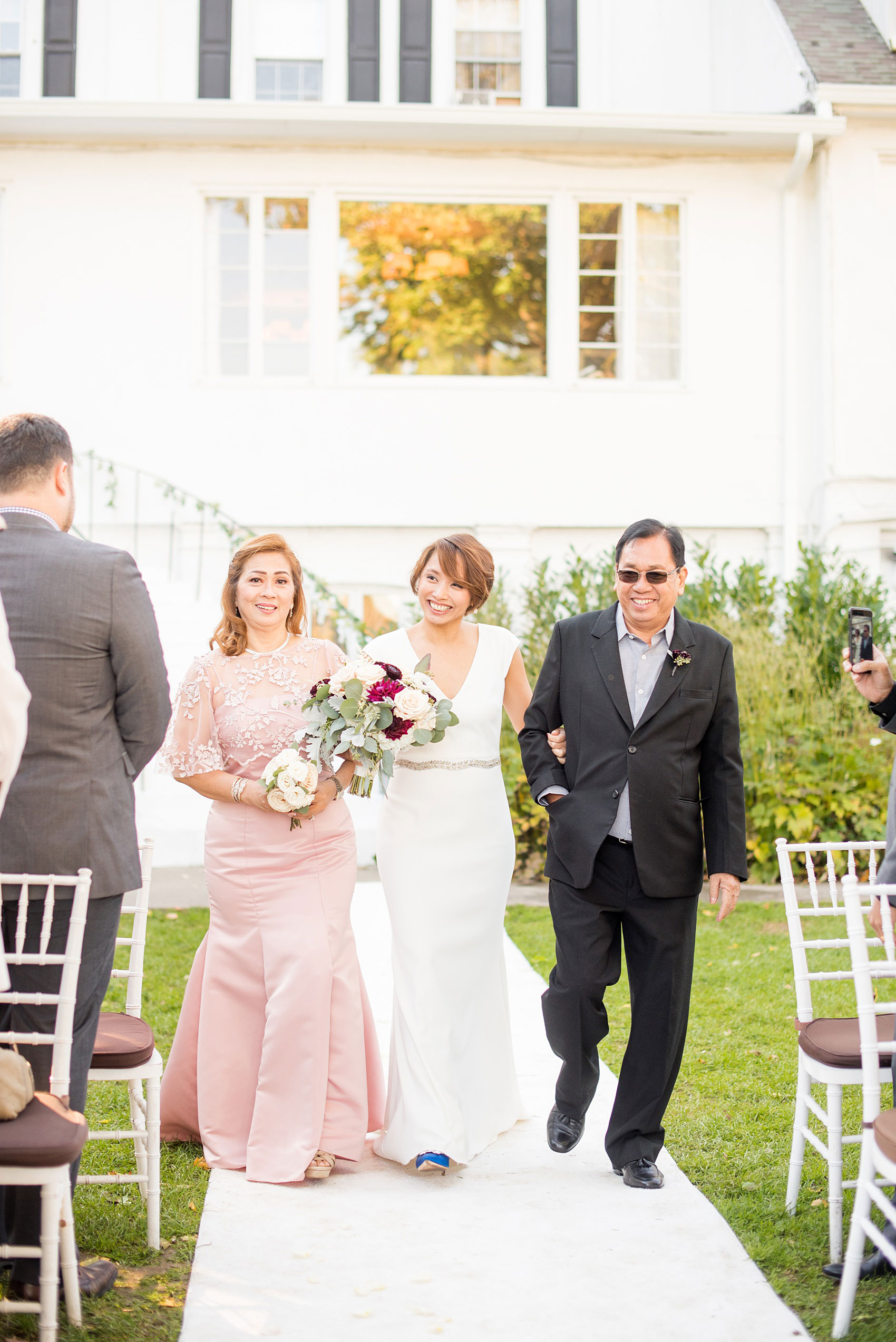 Mikkel Paige Photography photos of a wedding at Crabtree's Kittle House in Chappaqua, New York. Picture of the bride's parents walking her down the aisle for their outdoor fall ceremony. 