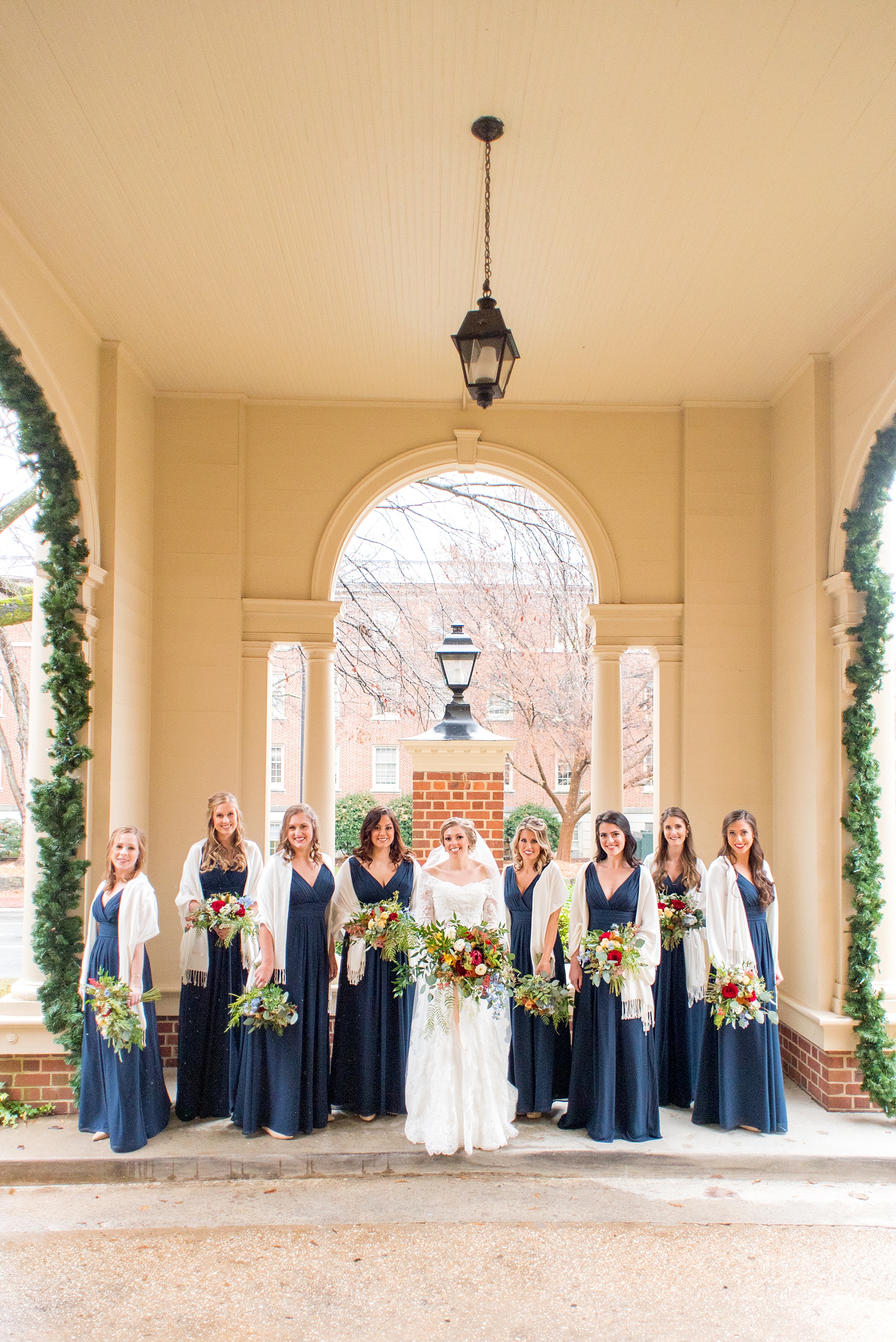 Beautiful wedding photos at The Carolina Inn at Chapel Hill, North Carolina by Mikkel Paige Photography. Photo of the bridal party in navy blue gowns with winter colorful bouquets and white shawls. Click through to see the rest of this gorgeous winter wedding! #thecarolinainn #snowywedding