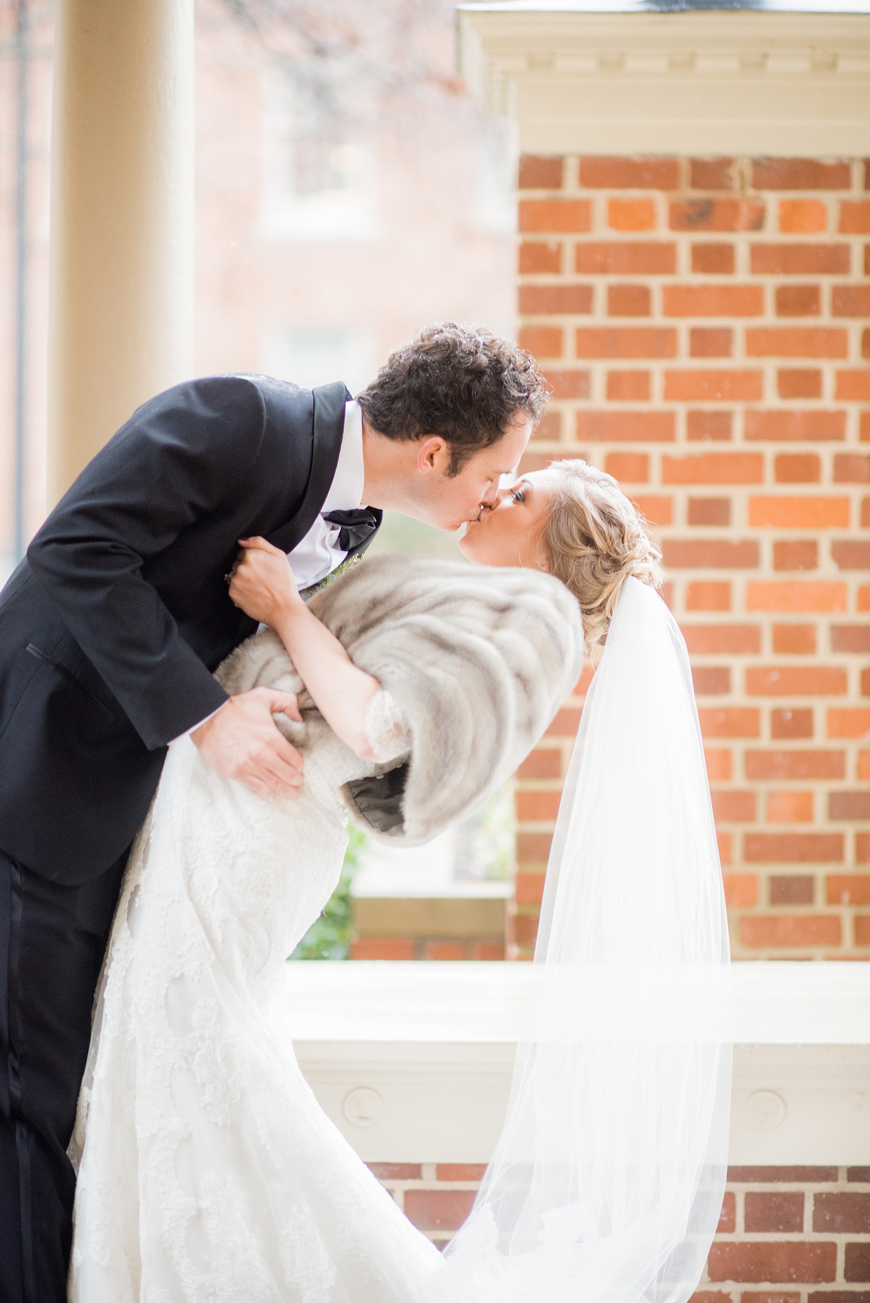 Beautiful wedding photos at The Carolina Inn at Chapel Hill, North Carolina by Mikkel Paige Photography. Photo of the bride in her heirloom fur shawl and veil kissing her groom in a black tuxedo. #thecarolinainn #snowywedding