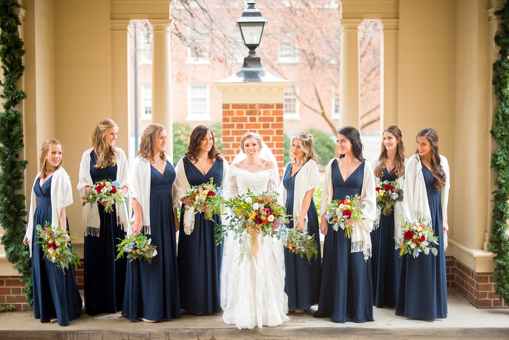 Beautiful wedding photos at The Carolina Inn at Chapel Hill, North Carolina by Mikkel Paige Photography. Photo of the bridal party in navy blue gowns with winter colorful bouquets and white shawls. Click through to see the rest of this gorgeous winter wedding! #thecarolinainn #snowywedding