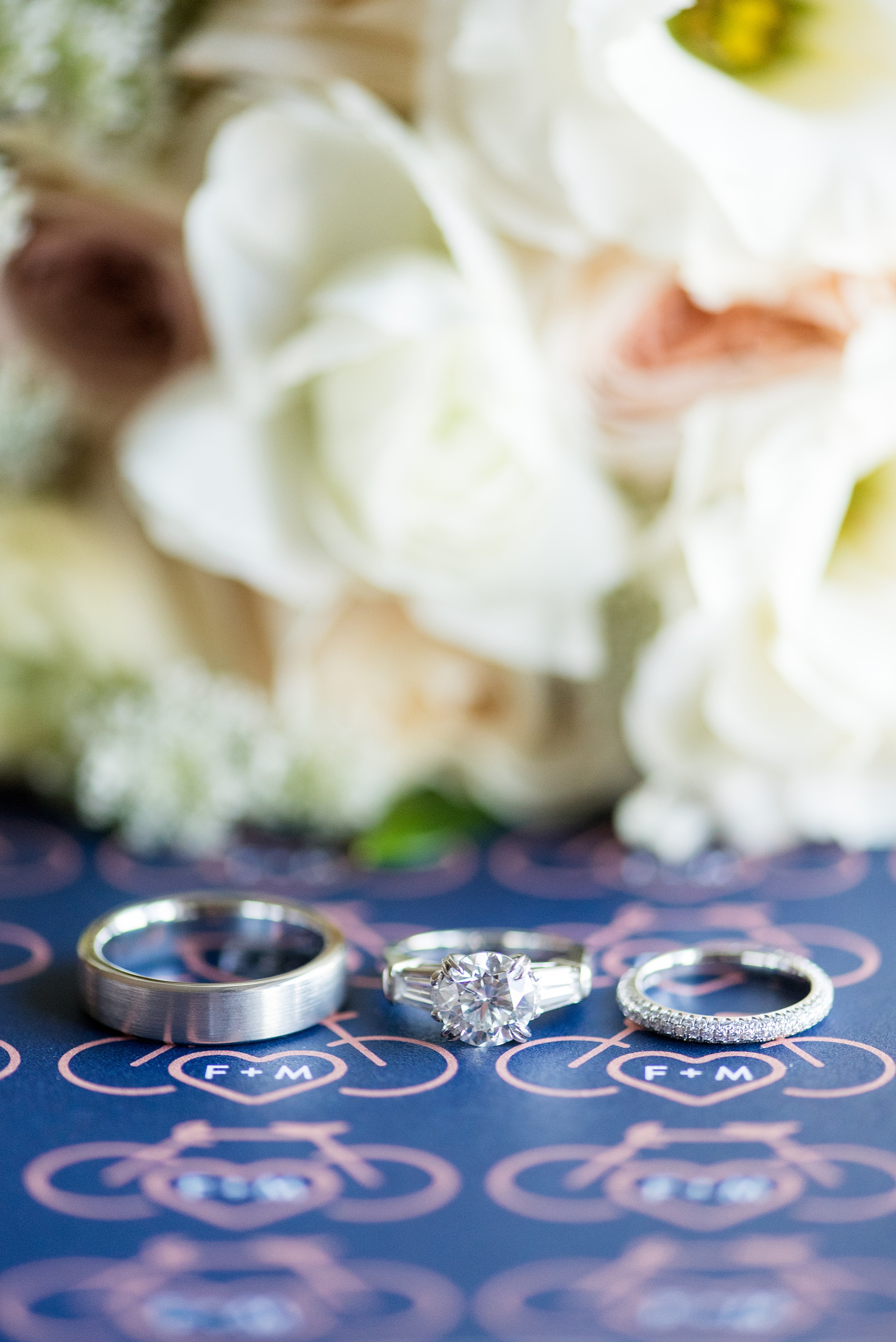 Photos by Mikkel Paige Photography of a Central Park Wedding ceremony and reception at the Loeb Boathouse venue with a romantic theme. Detail picture of the bride and groom's white gold wedding and diamond engagement rings against their custom bicycle monogram design. Click through for more images from her day! #CentralParkWedding