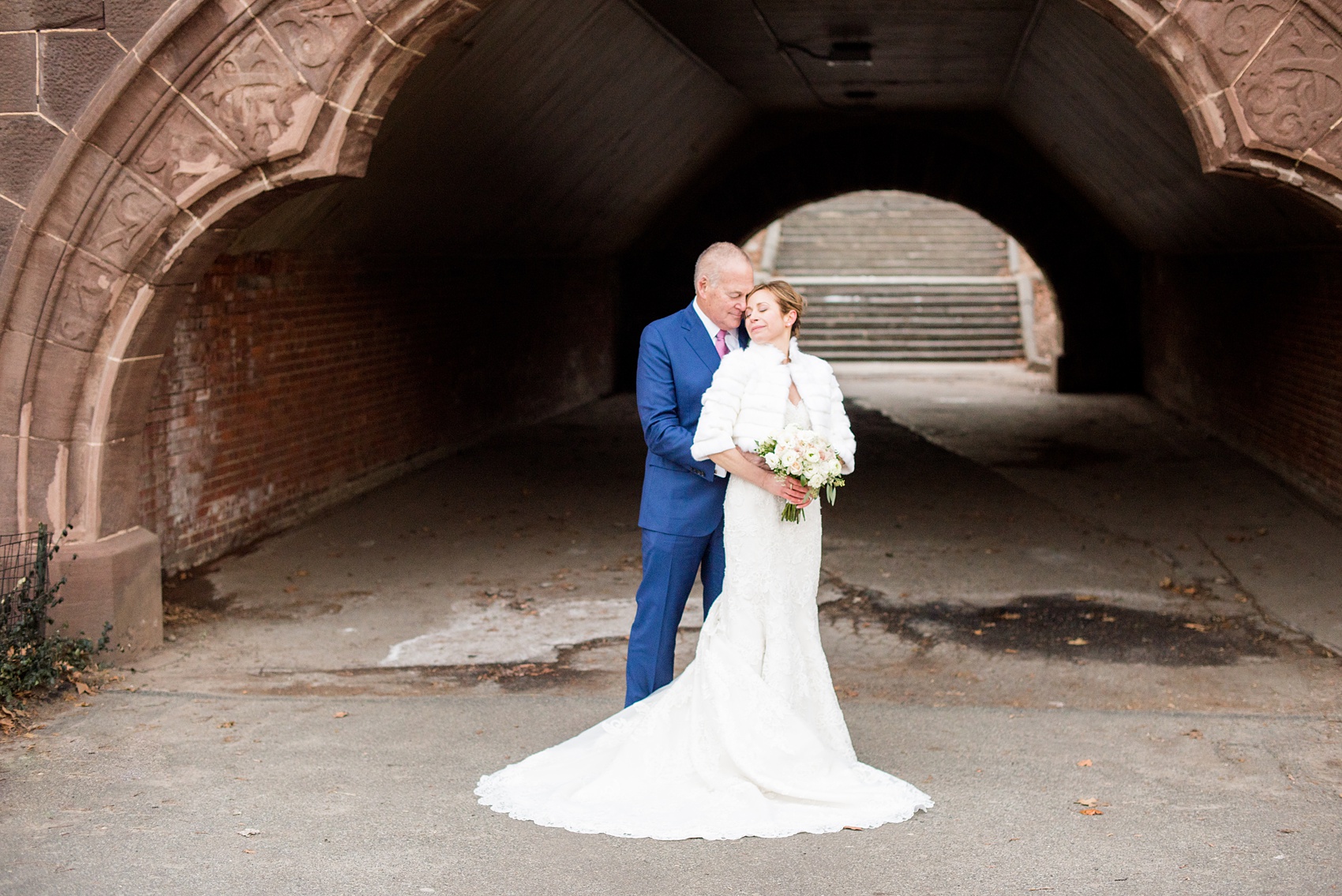 Photos by Mikkel Paige Photography of a Central Park Wedding ceremony and reception at the Loeb Boathouse venue with a romantic winter theme. The bride and groom took pictures around the park in his custom navy blue suit and her lace gown with short white fur coat. Click through for more images from their day! #CentralParkWedding