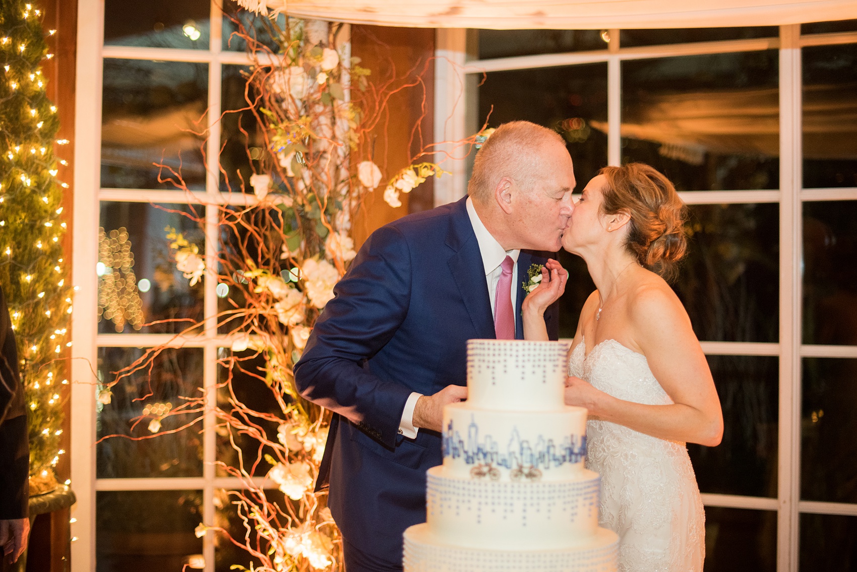 Photos by Mikkel Paige Photography of a Central Park Wedding reception at the Loeb Boathouse venue with a romantic winter theme. Picture of the tiered white wedding cake cutting with NYC skyline piped in blue and two bicycles for the bride and groom. Click through for more images from this beautiful day! #CentralParkWedding