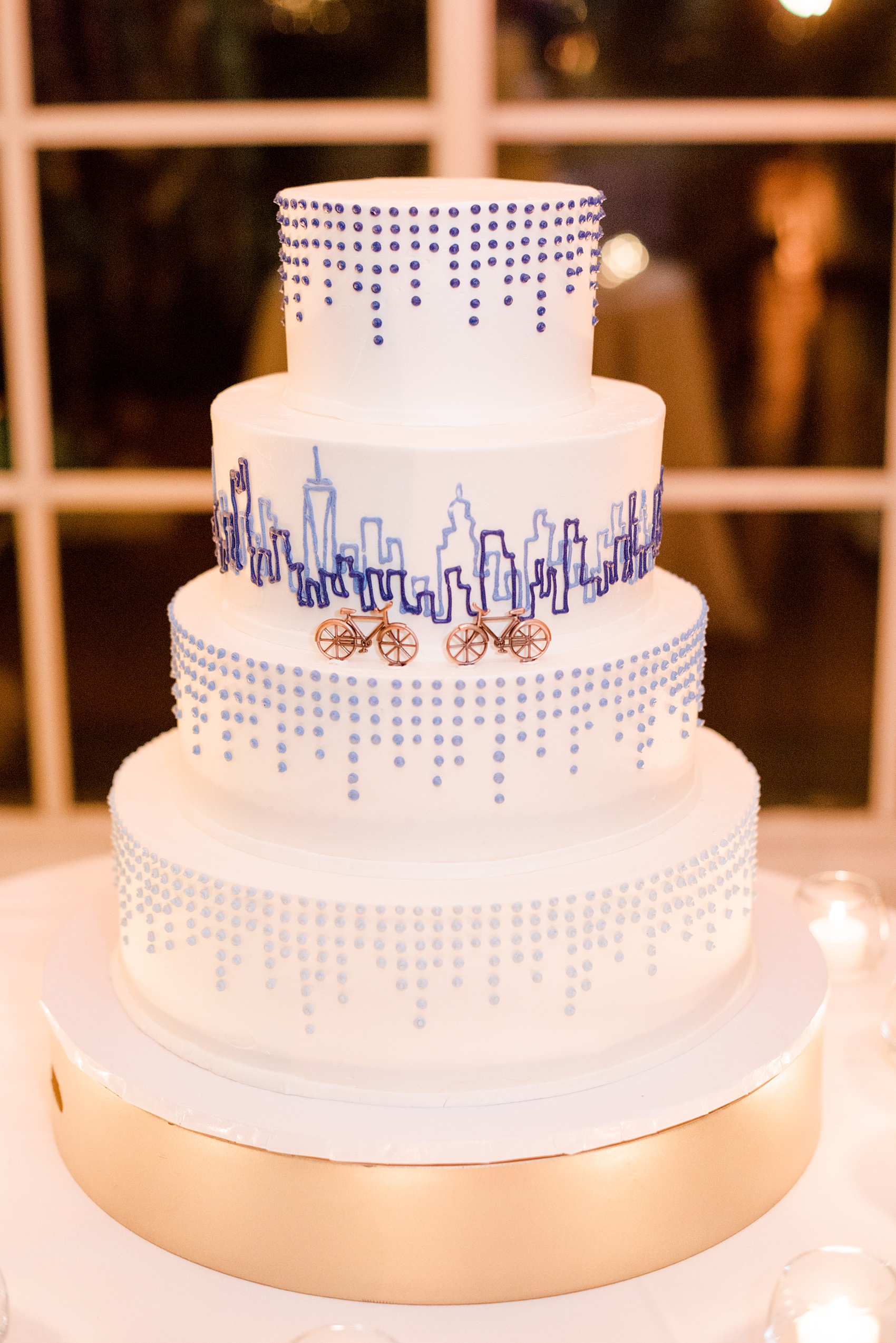 Photos by Mikkel Paige Photography of a Central Park Wedding reception at the Loeb Boathouse venue with a romantic winter theme. Picture of the tiered white wedding cake with NYC skyline piped in blue and two bicycles for the bride and groom. Click through for more images from this beautiful day! #CentralParkWedding