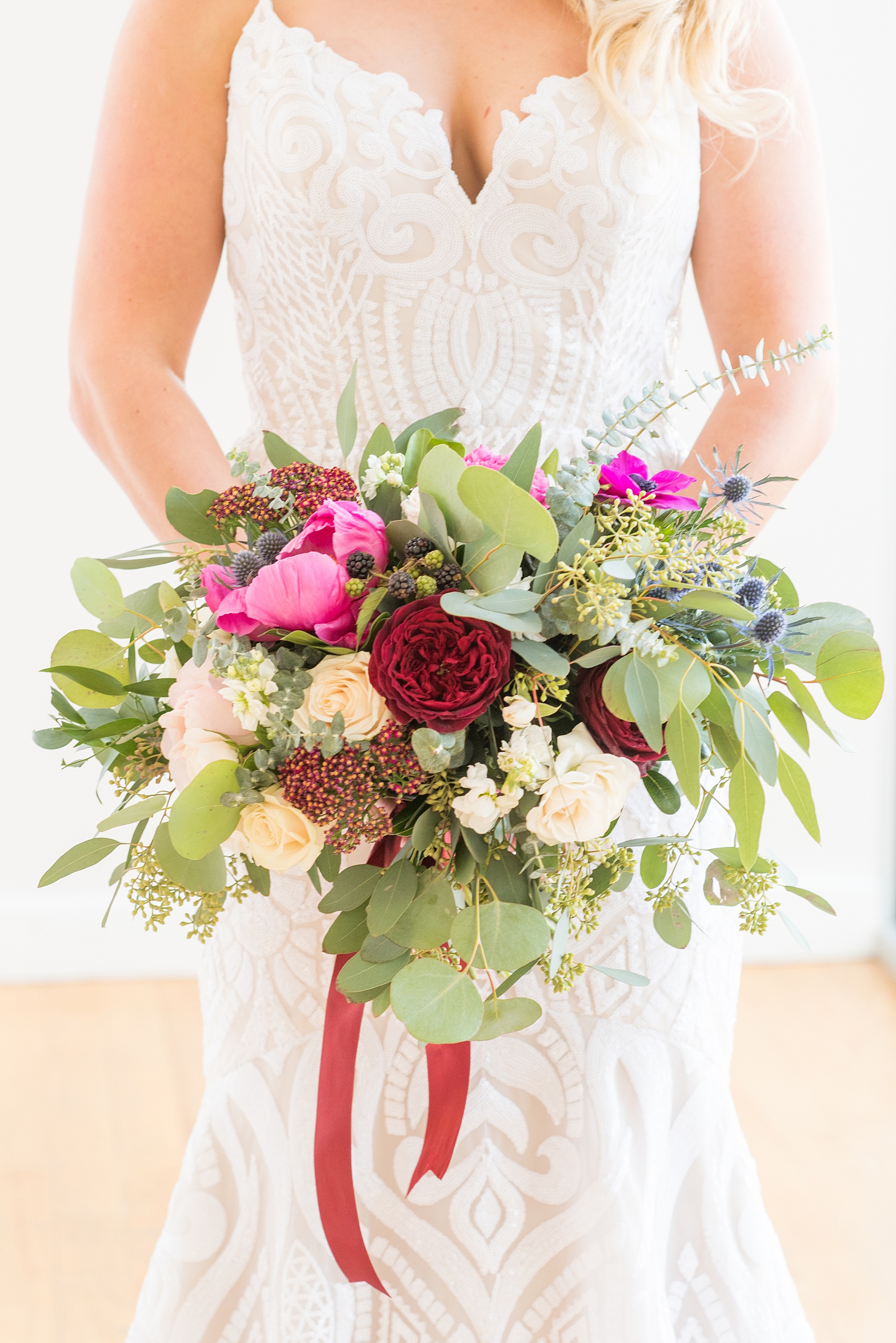 Photos from a wedding in downtown Raleigh, NC by Mikkel Paige Photography. The Stockroom at 230 and The Glass Box on historic Fayetteville Street served as the venue for this romantic inspiration shoot. The bride carried an organic inspired bouquet with fuchsia peonies, blue thistle, burgundy roses and a pink anemone. Silver dollar eucalyptus filled in the flowers tied by maroon ribbons, by Tre Bella.