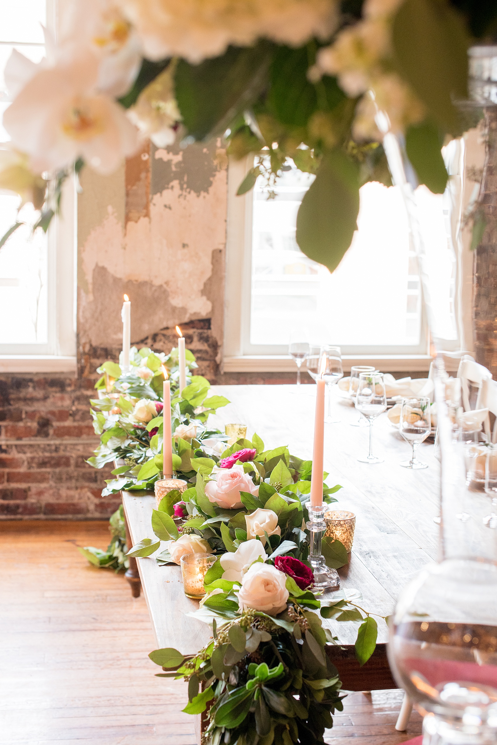 Photos from a wedding in downtown Raleigh, NC by Mikkel Paige Photography. The reception was held at The Stockroom at 230, and the bridal party sat at a natural wood farm table with candlelight and greenery garland complete with colorful flowers. 