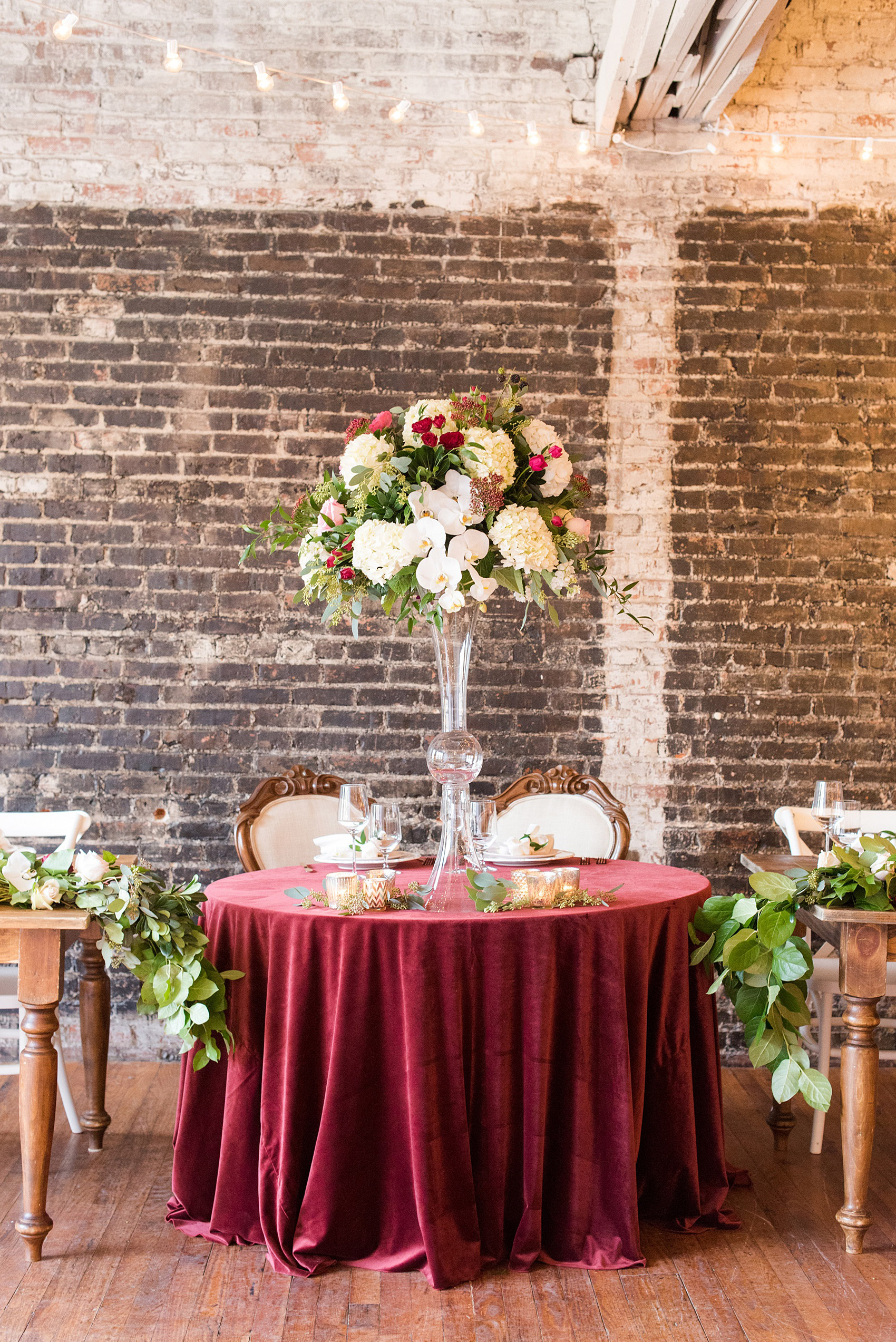 Photos from a wedding in downtown Raleigh, NC by Mikkel Paige Photography. The reception was held at The Stockroom at 230, and the sweetheart table was placed in front of the vintage brick. A red velvet linen completed the romantic table.