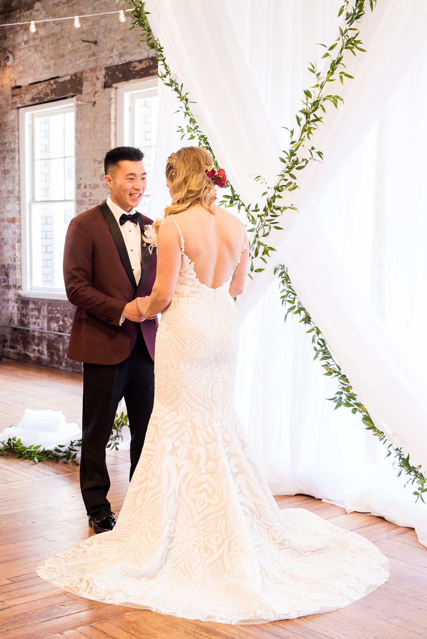 Photos from a wedding in downtown Raleigh, NC by Mikkel Paige Photography. The ceremony was held inside the historic venue, The Stockroom at 230, with white drapery and green garland hung up behind the bride and groom as they exchanged vows.