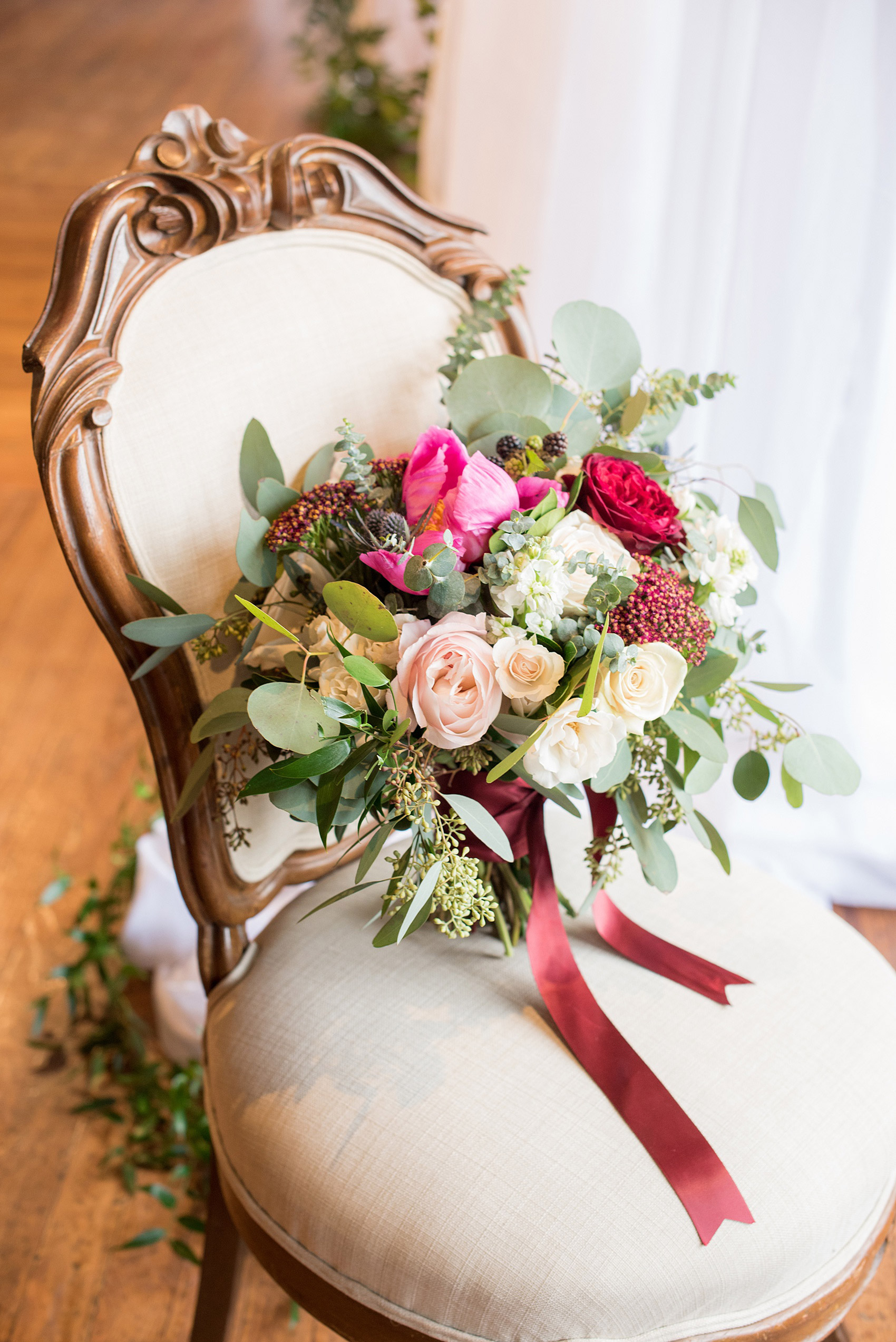 Photos from a wedding in downtown Raleigh, NC by Mikkel Paige Photography. The Stockroom at 230 and The Glass Box on historic Fayetteville Street served as the venue for this romantic inspiration shoot. The bride carried an organic inspired bouquet with fuchsia peonies, blue thistle, burgundy roses and a pink anemone. Silver dollar eucalyptus filled in the flowers tied by maroon ribbons, by Tre Bella.