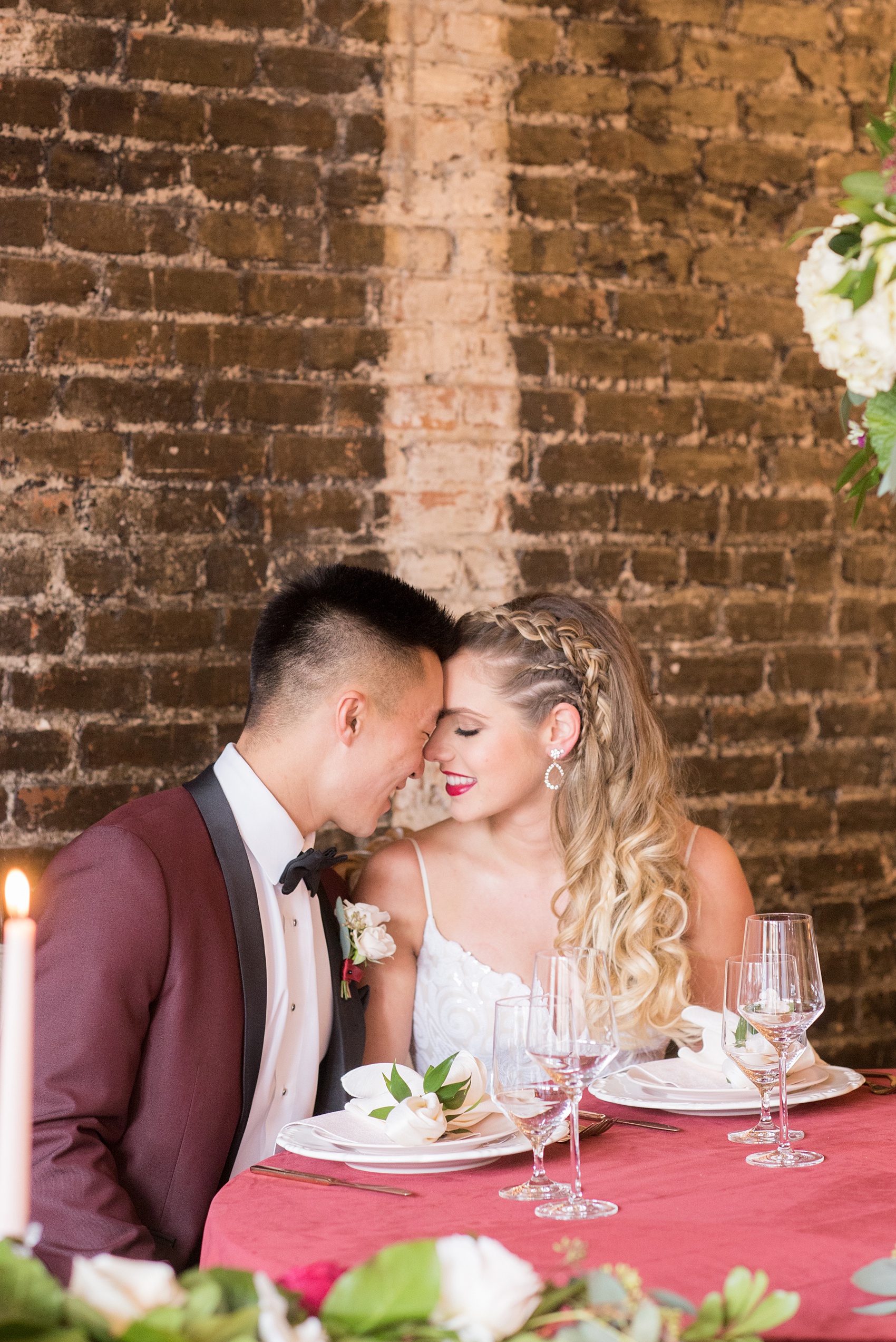 Photos from a wedding in downtown Raleigh, NC by Mikkel Paige Photography. The ceremony was held inside the historic venue, The Stockroom at 230. The bride and groom cuddled at their sweetheart table, complete with a velvet maroon linen, pink champagne flutes and pink details.